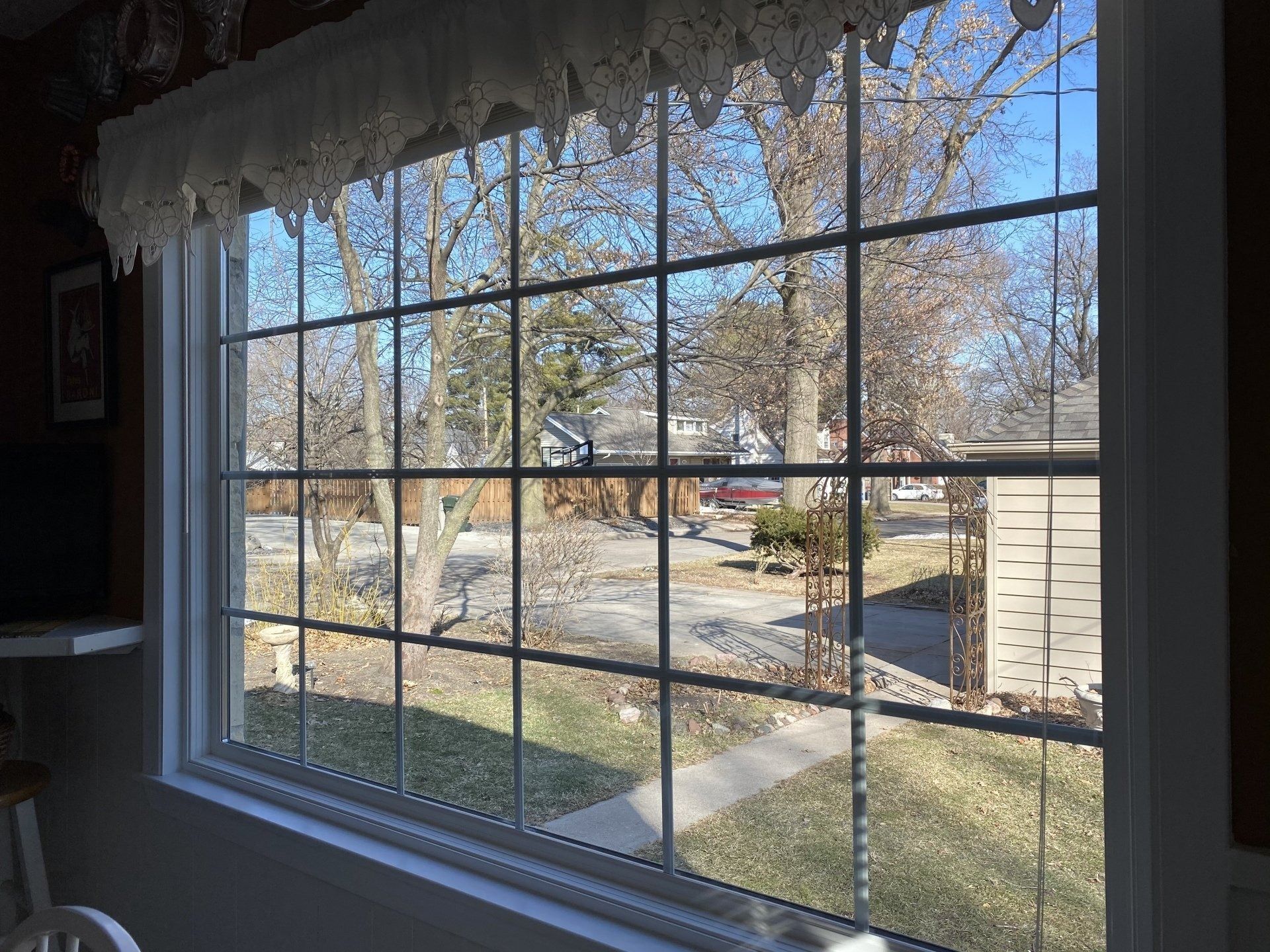Window view of a street with bare trees, houses, and a building on a sunny day.