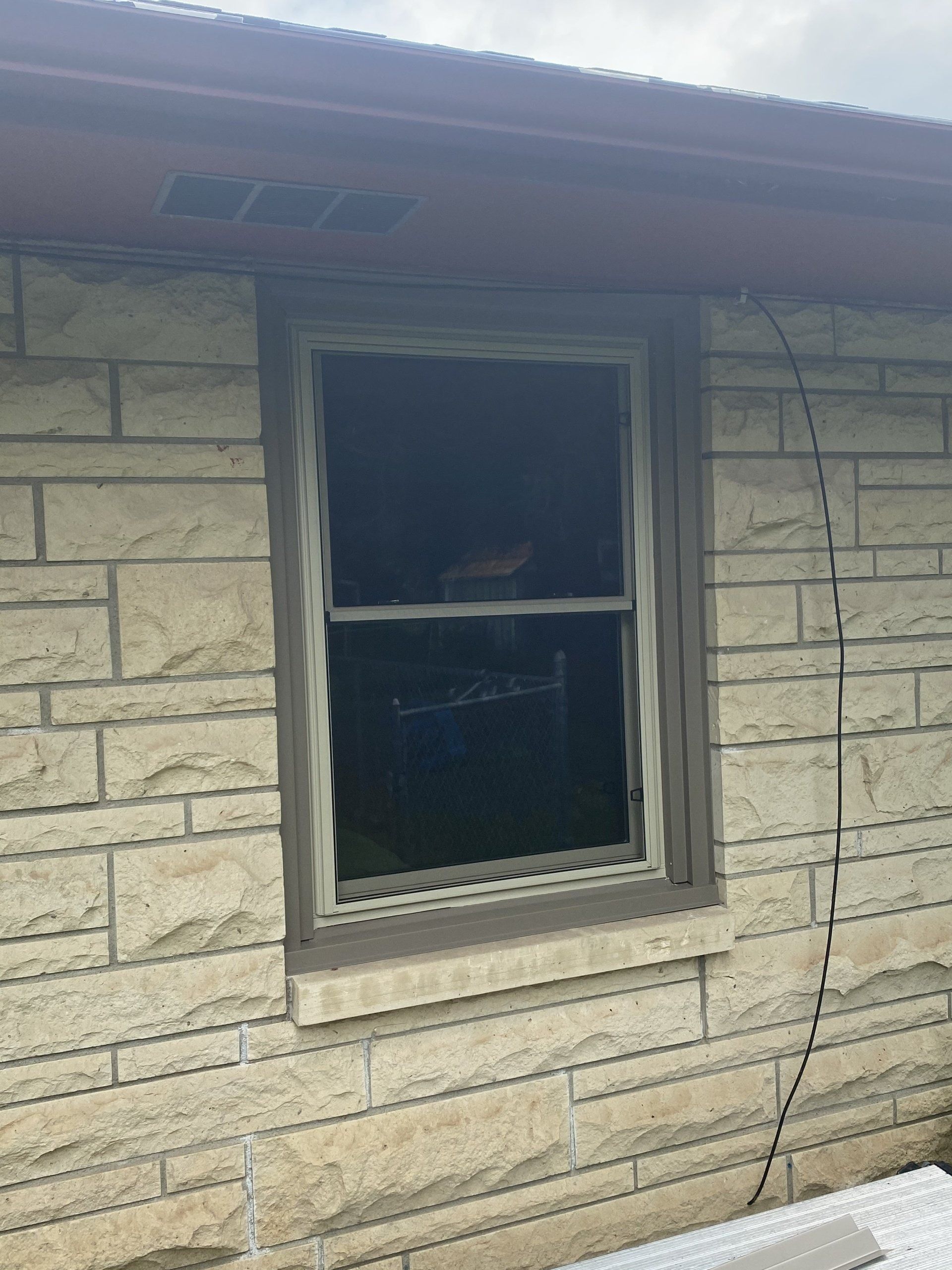 Window on a stone wall, framed in brown, with a dark interior; beige brick exterior.
