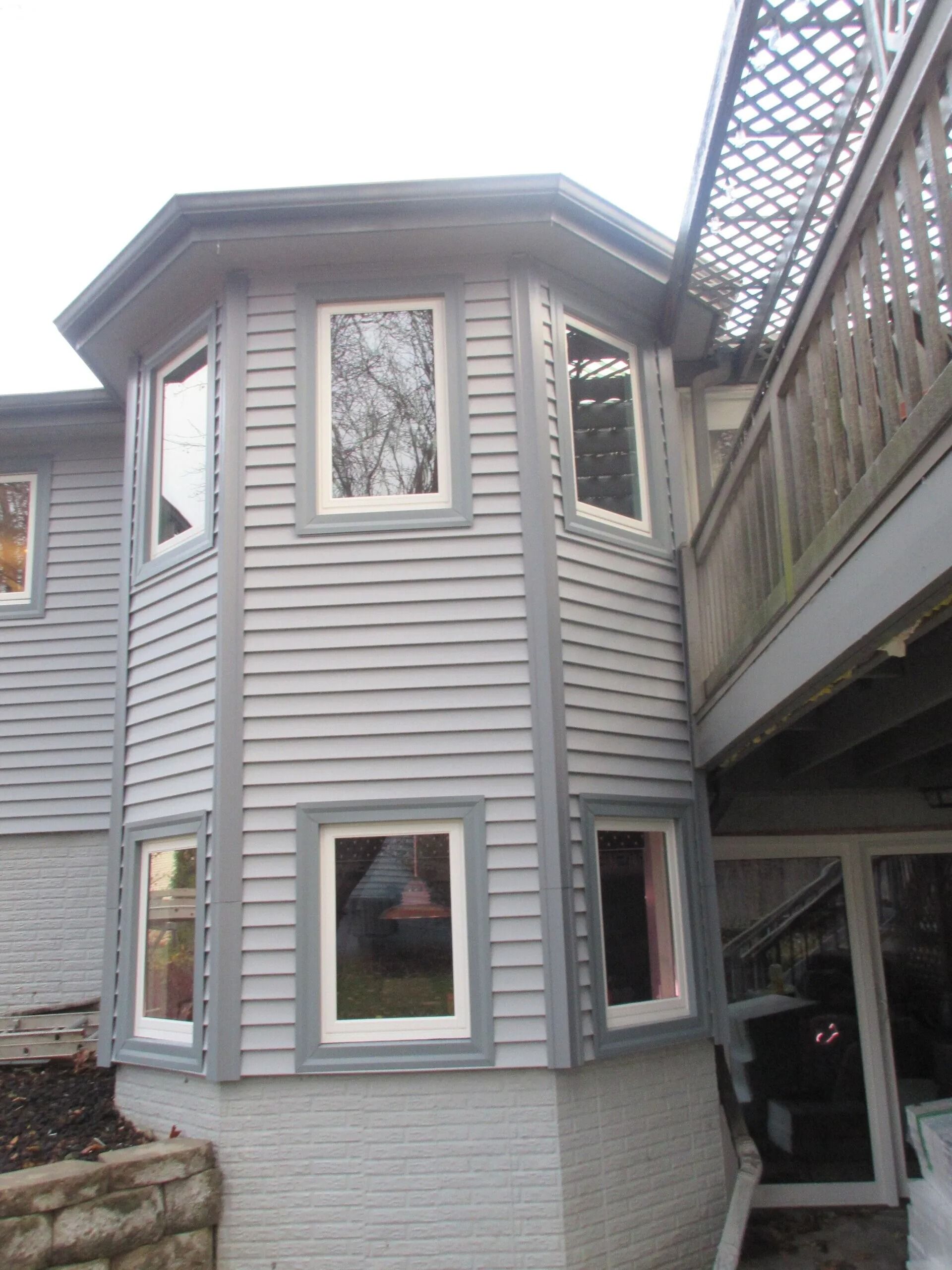 Exterior of a multi-story house with gray siding and windows. A wooden deck is attached to the upper floor.