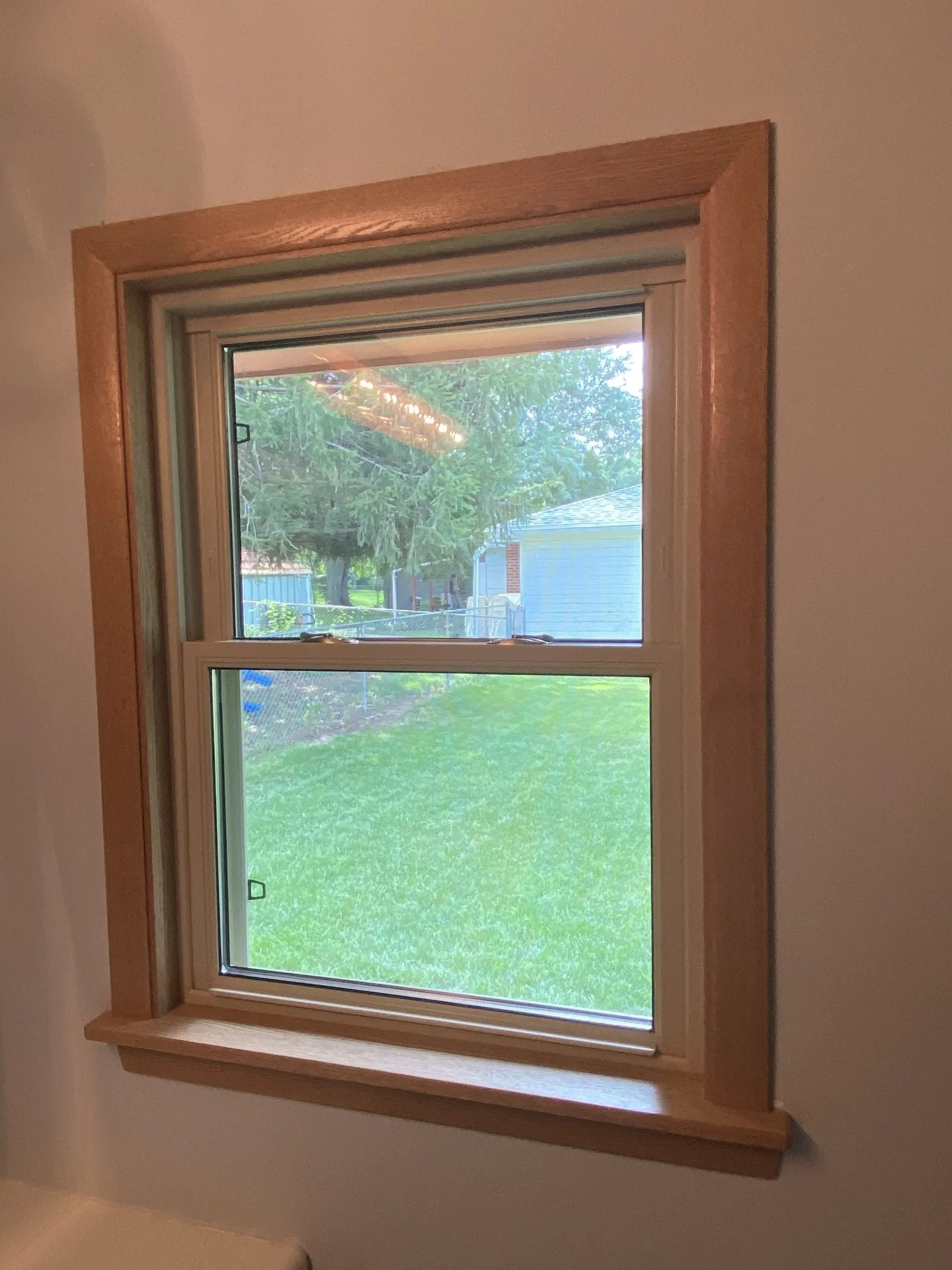 Wooden framed window, rectangular, in a room with a view of green grass and trees outside.