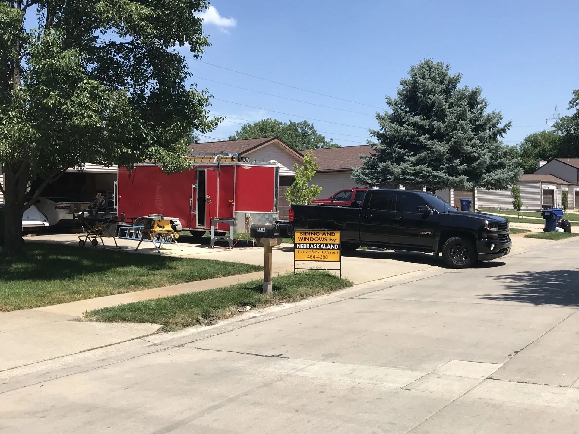 Black truck parked next to a red trailer on a residential street; construction work is in progress.