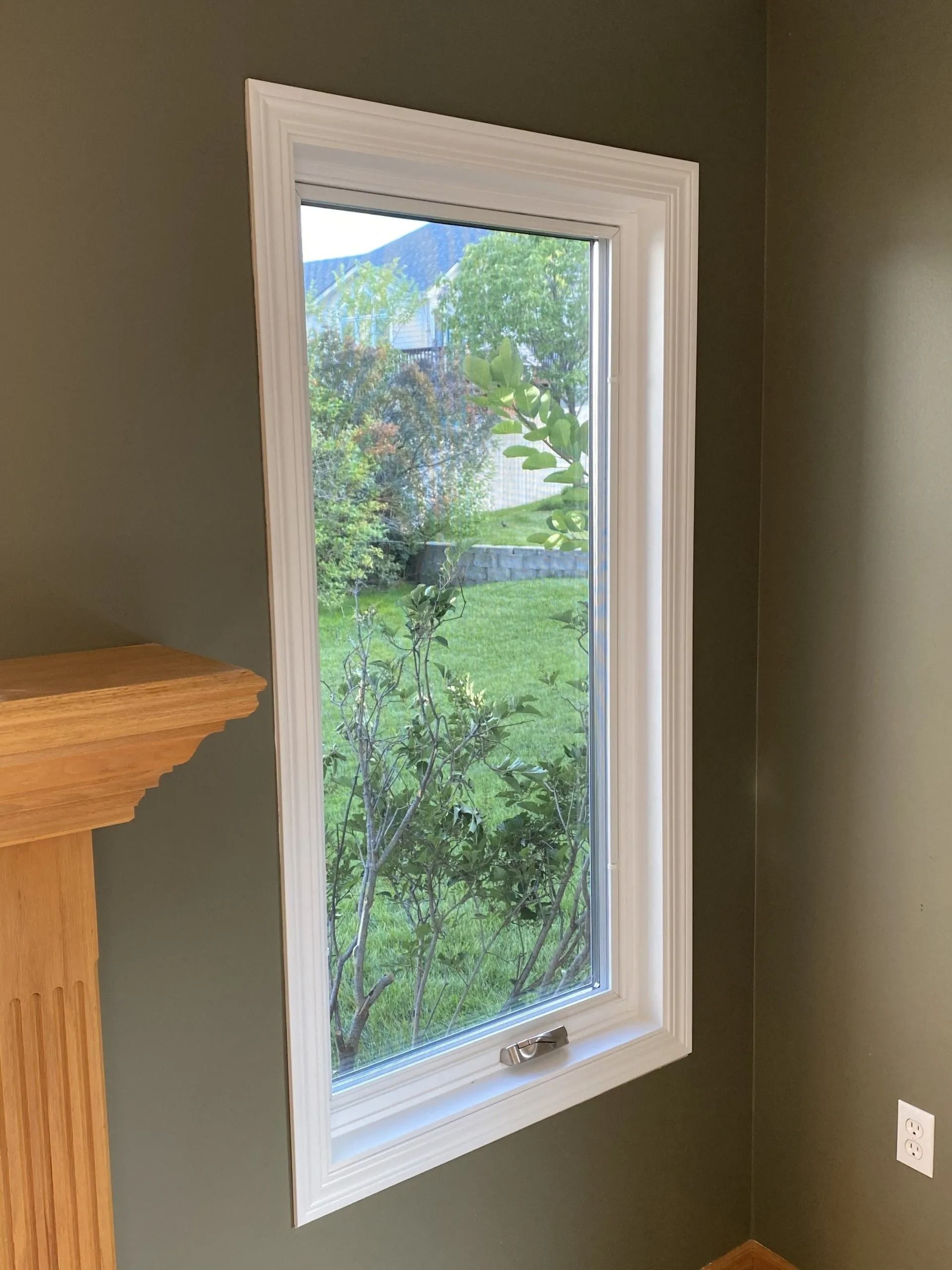 A tall, rectangular window with white trim in a room with green walls. A green outdoor view is visible through the window.