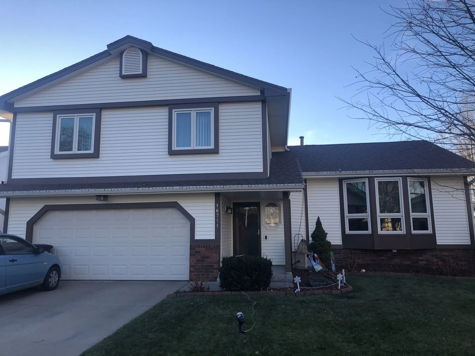 Two-story house with white siding, brown trim, and a two-car garage. A car is parked in the driveway.