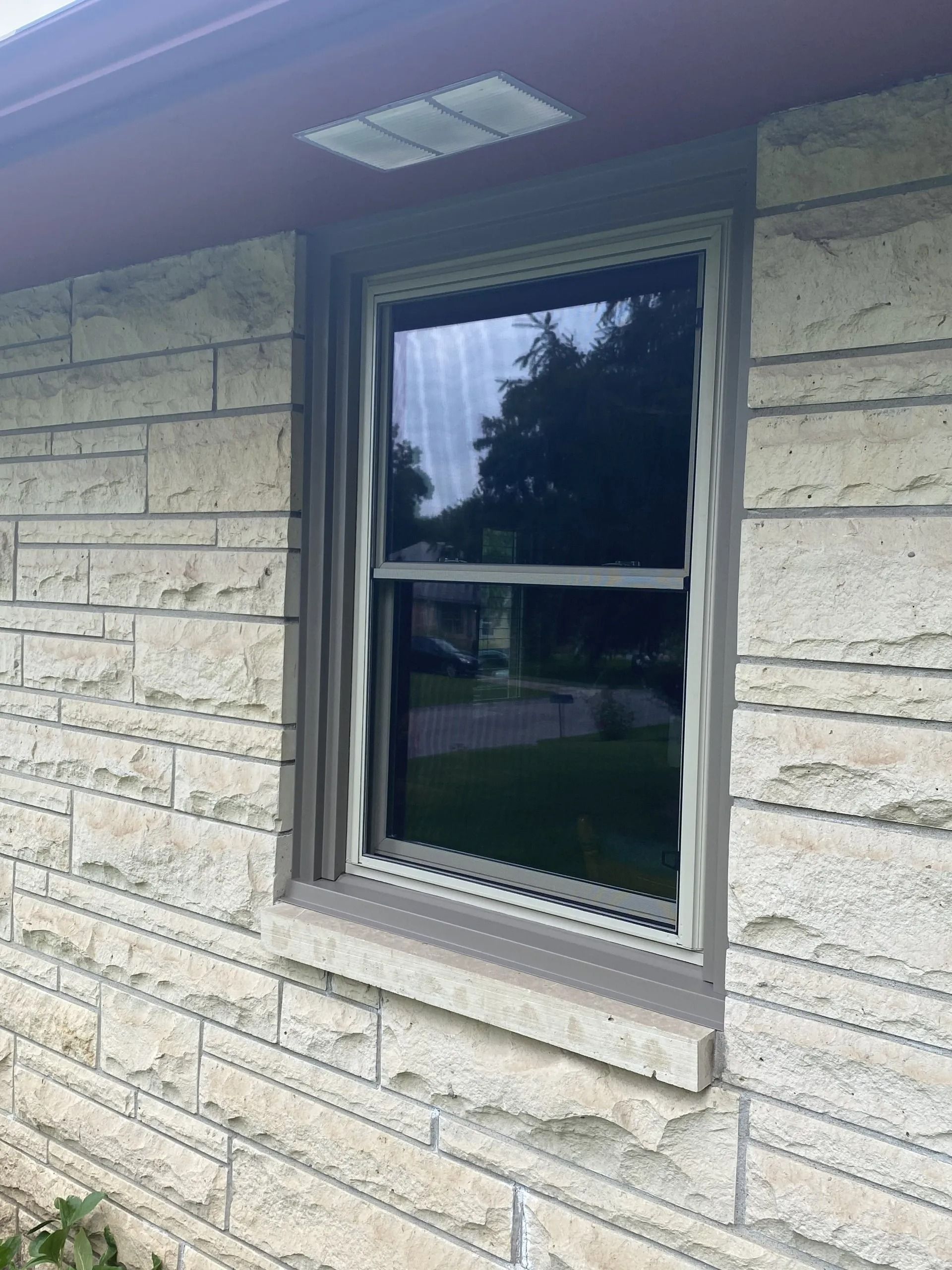 Single-hung window set in a light stone wall with a brown trim and a dark, reflective glass.