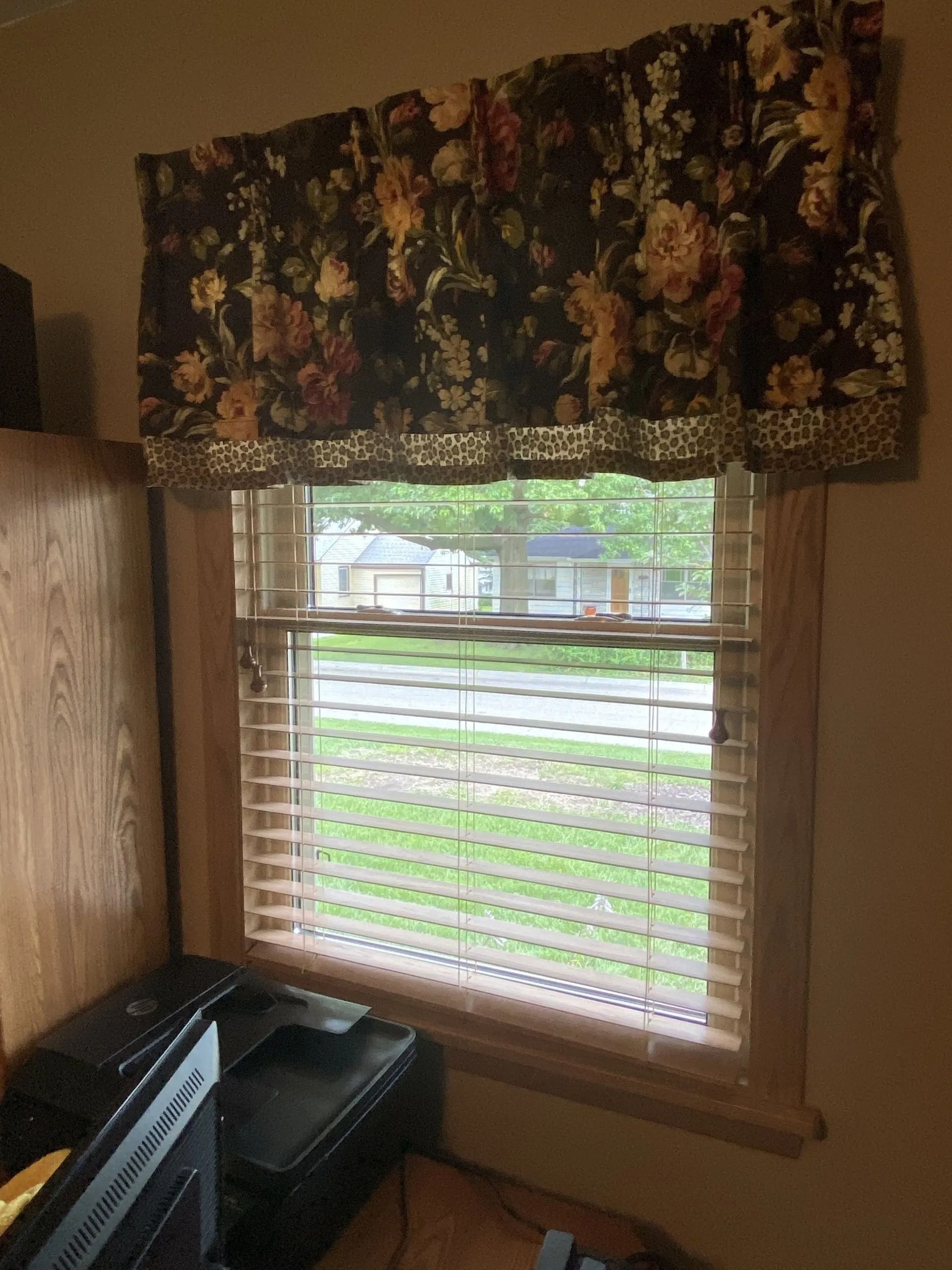 Window with floral valance and blinds, view of street outside.
