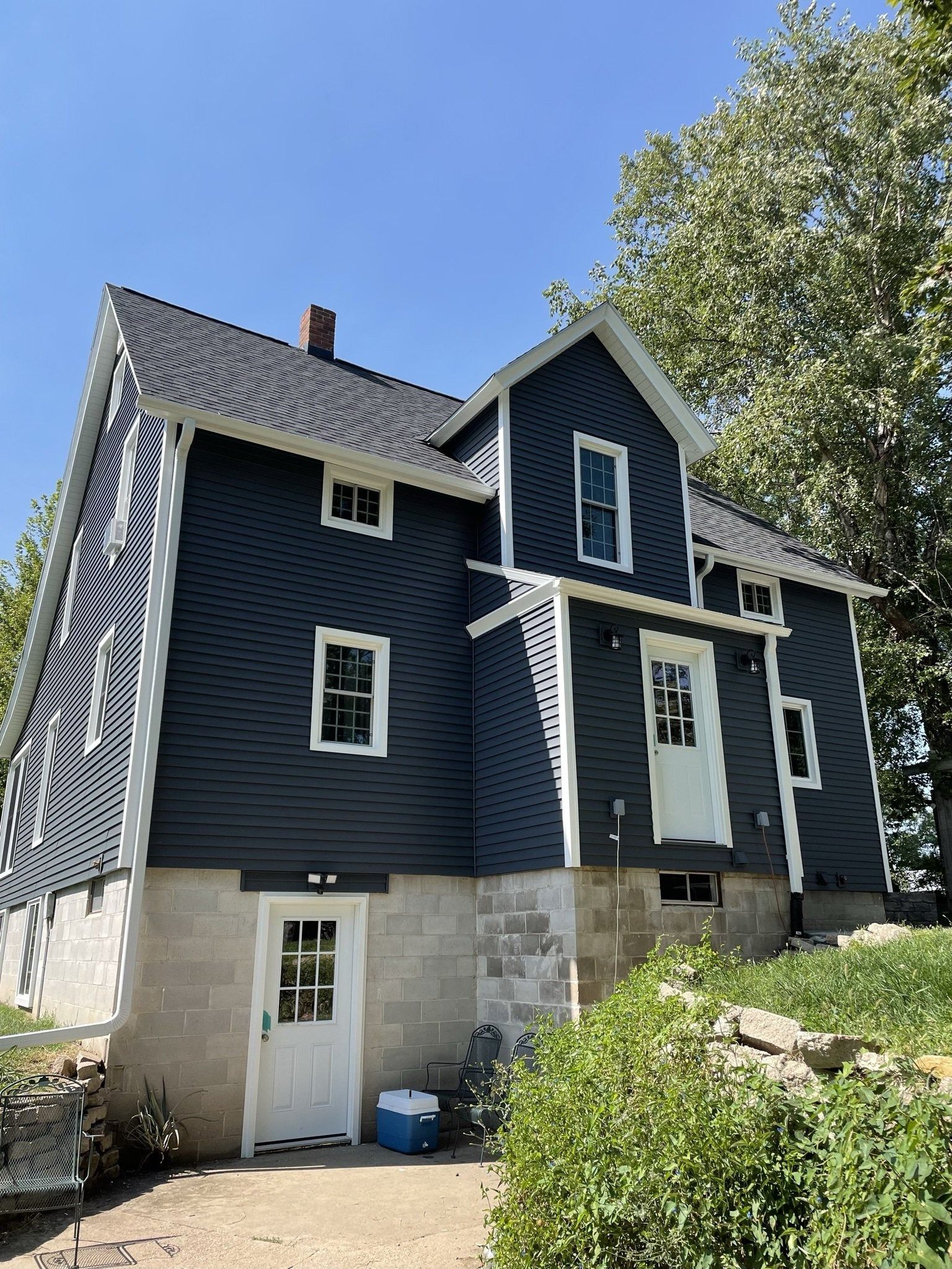 Dark blue house with white trim and a stone foundation against a blue sky.