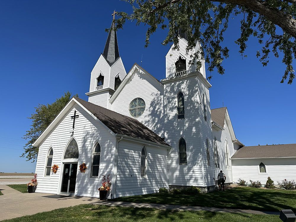 White church with two spires under a blue sky, framed by tree branches.