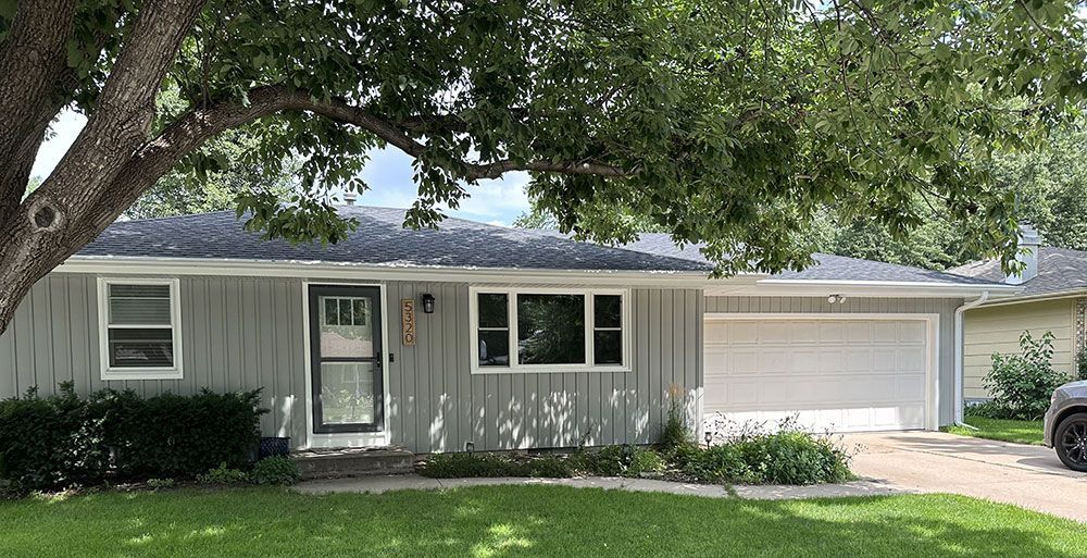 Gray ranch-style house with a tree in front. Features include a garage, front door, and windows.