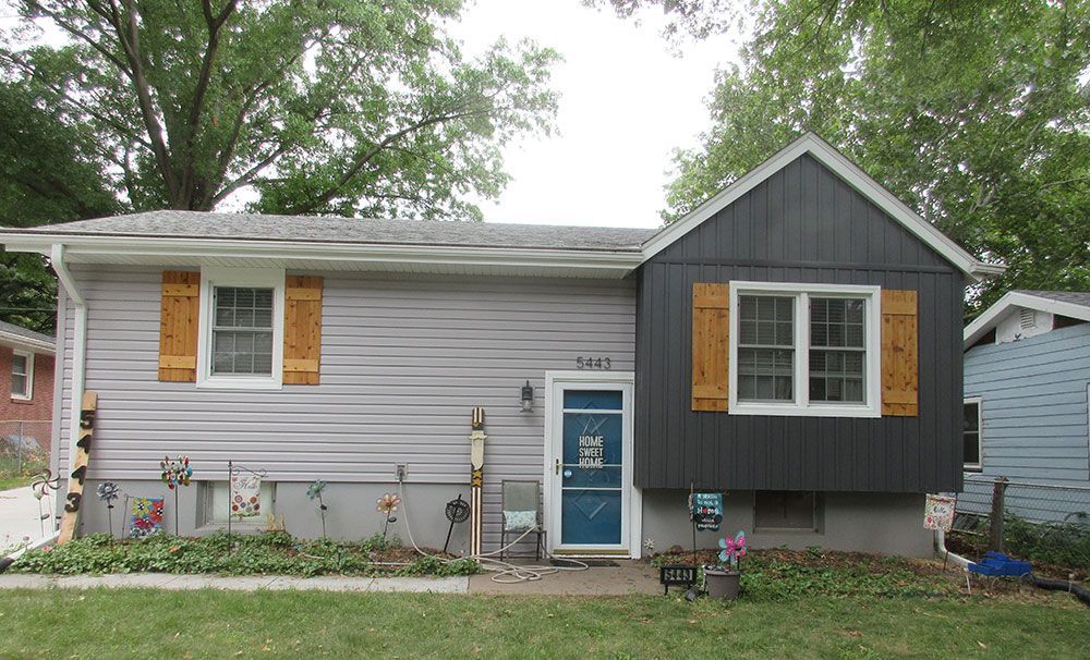 Gray house with wood shutters and dark gray accent. Blue door.