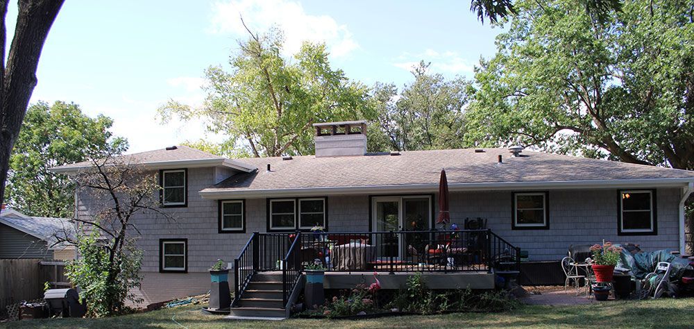 Backyard view of a two-story gray house with a deck, trees, and blue sky.