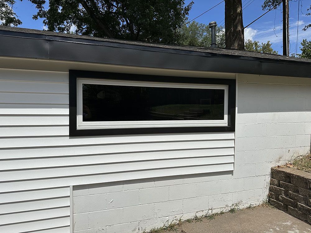 White siding building with a black-framed window and trim. Dark roof, daytime.