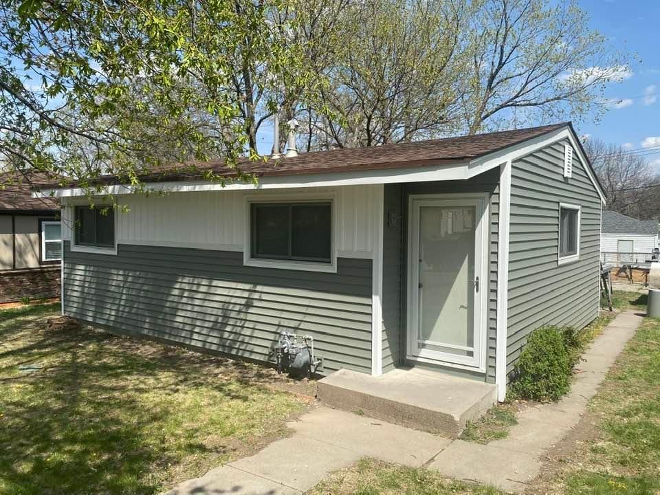 Small house with gray and white siding, front door, and concrete path.