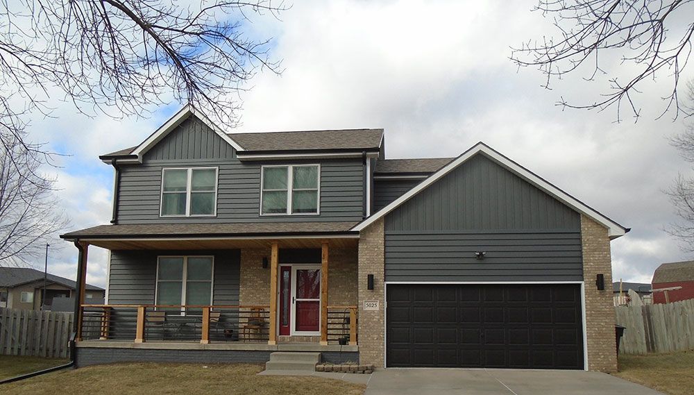 Two-story house with gray siding, brick accents, and a brown garage door under a cloudy sky.