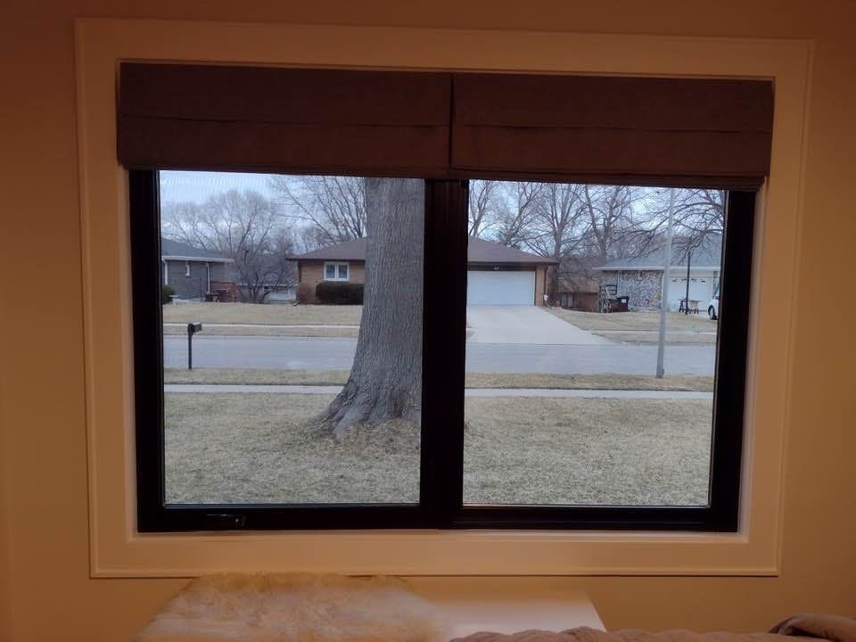 Window with a view of a street, houses, and a tree. Brown shades are above the window.