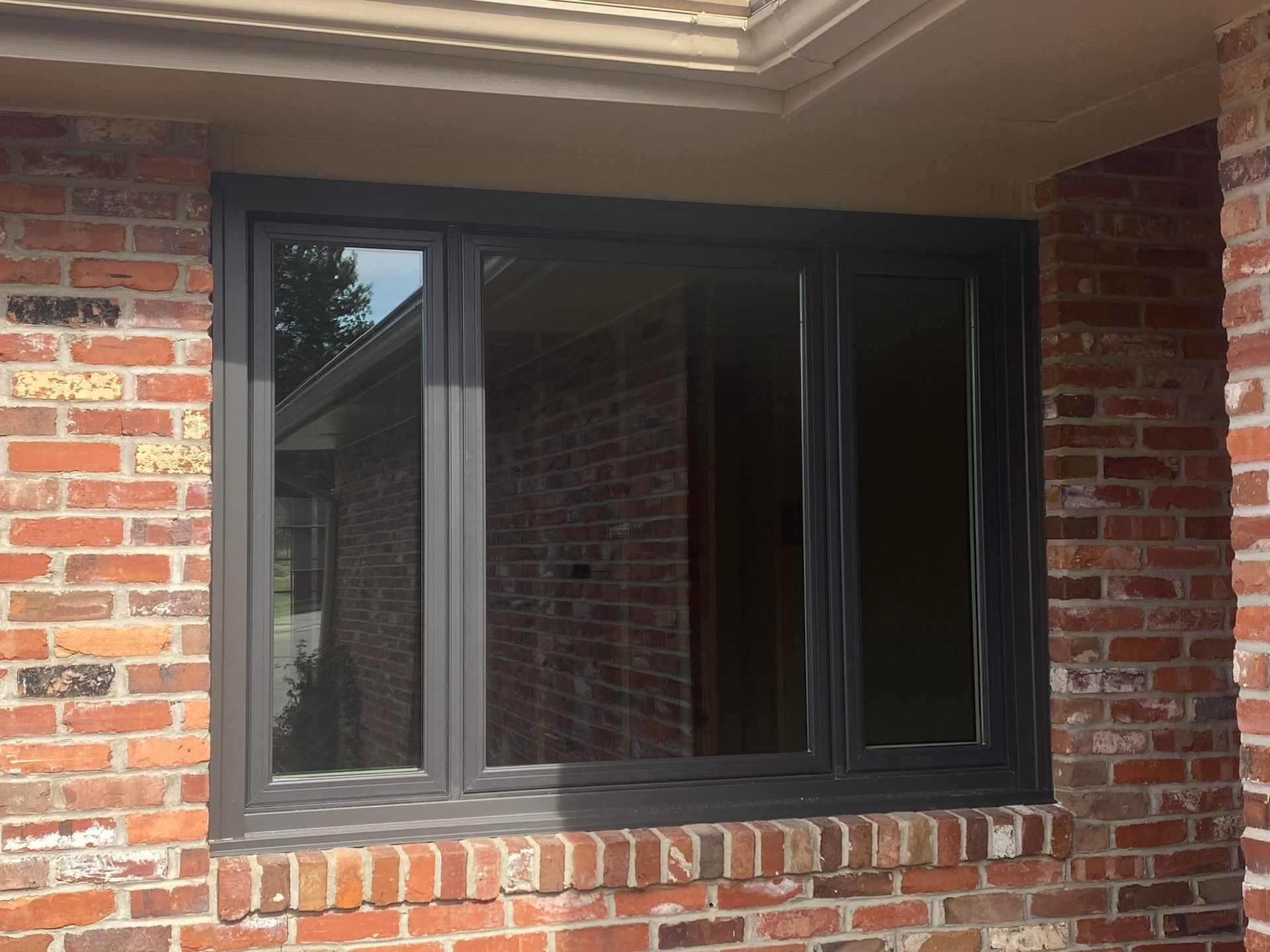 Gray-framed windows on a brick building exterior. Three window panes reflect a glimpse of the outdoors.