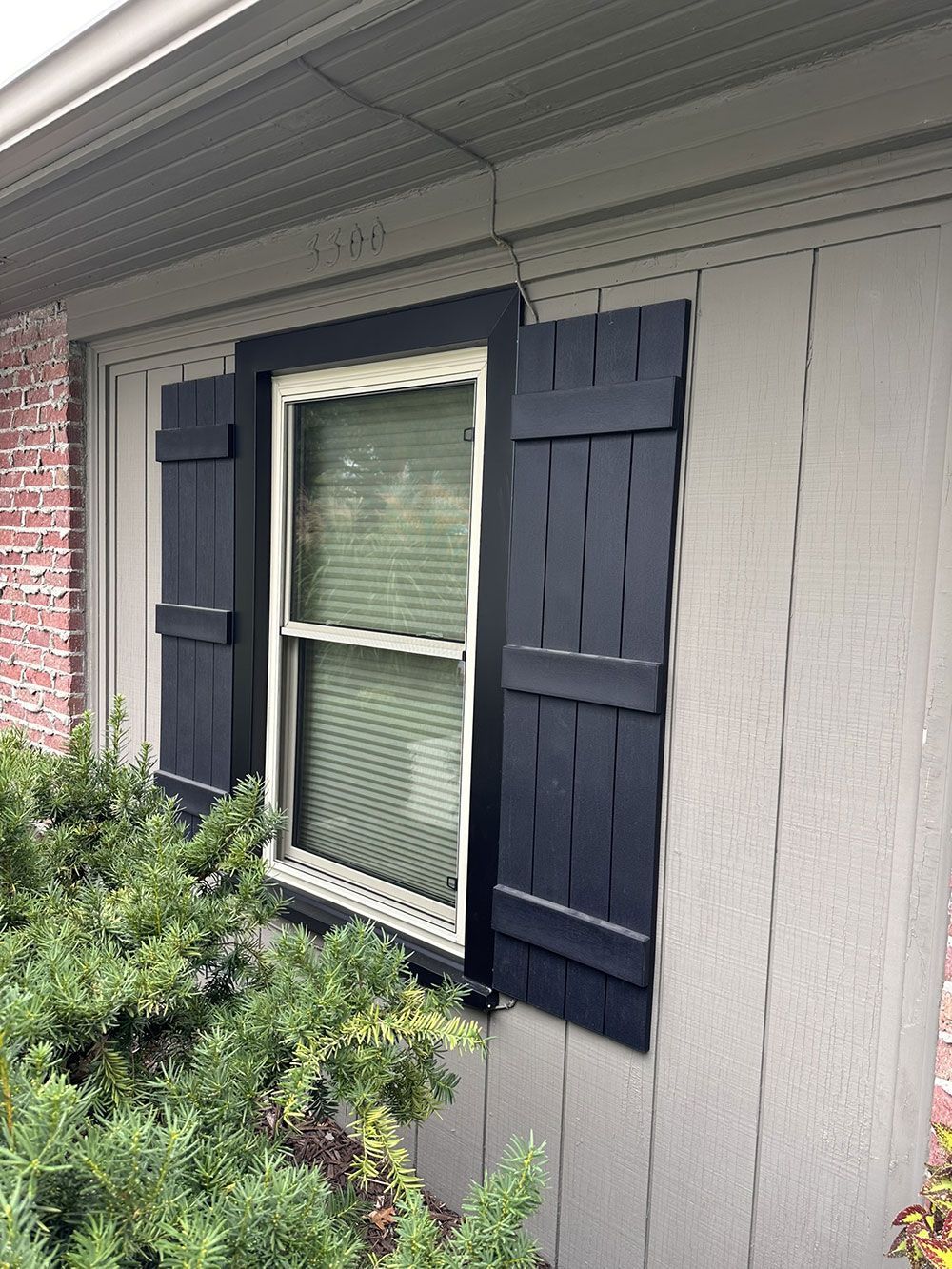 Dark blue shutters flank a window with white trim on a beige house exterior.