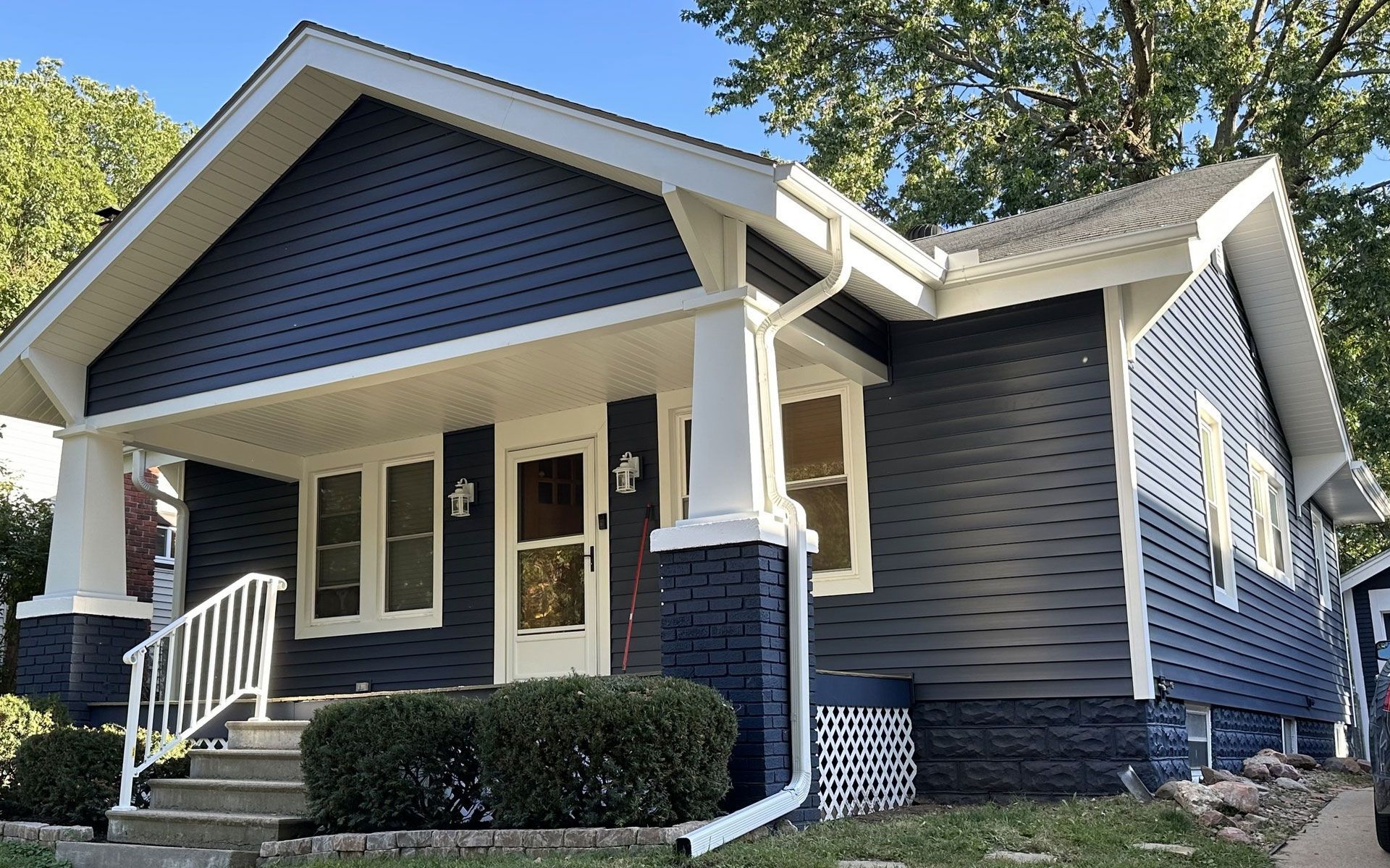 Blue and white Craftsman-style house with a front porch, bushes, and a gray staircase.