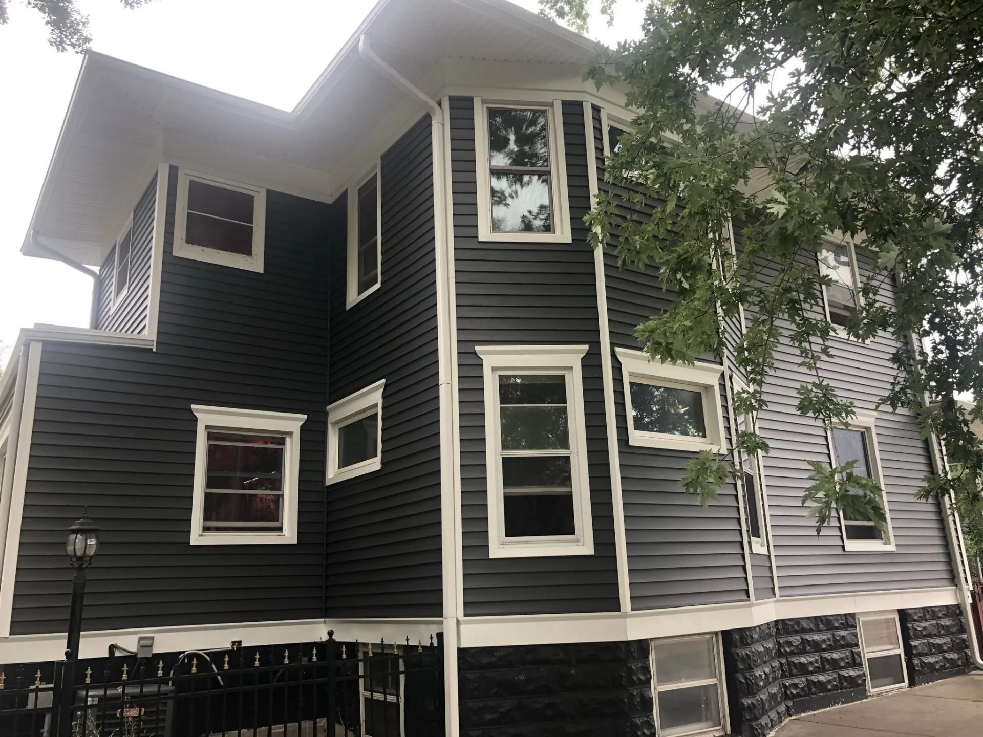 Two-story house with dark gray siding, white trim around windows, and a black foundation.