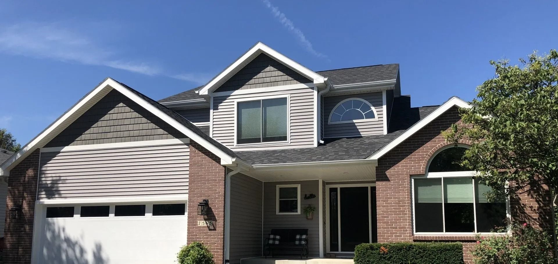 Two-story house with gray roof, brick and gray siding, white trim, and a blue sky.