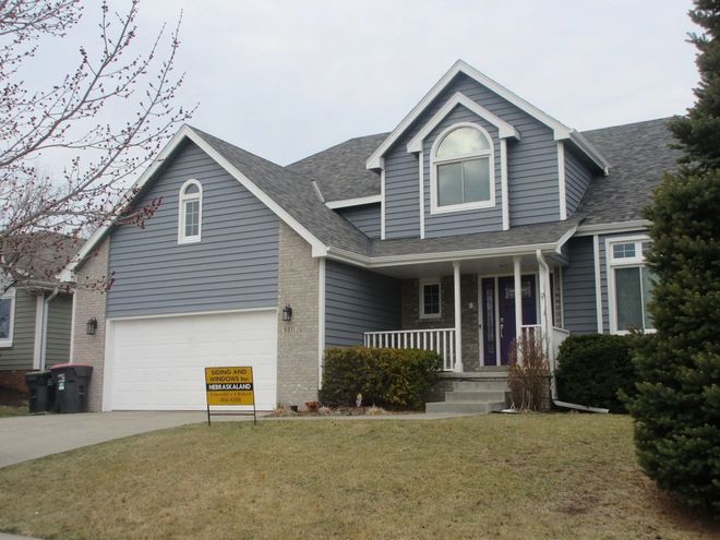 Two-story house with blue siding, gray roof, white garage door, and a brown lawn.