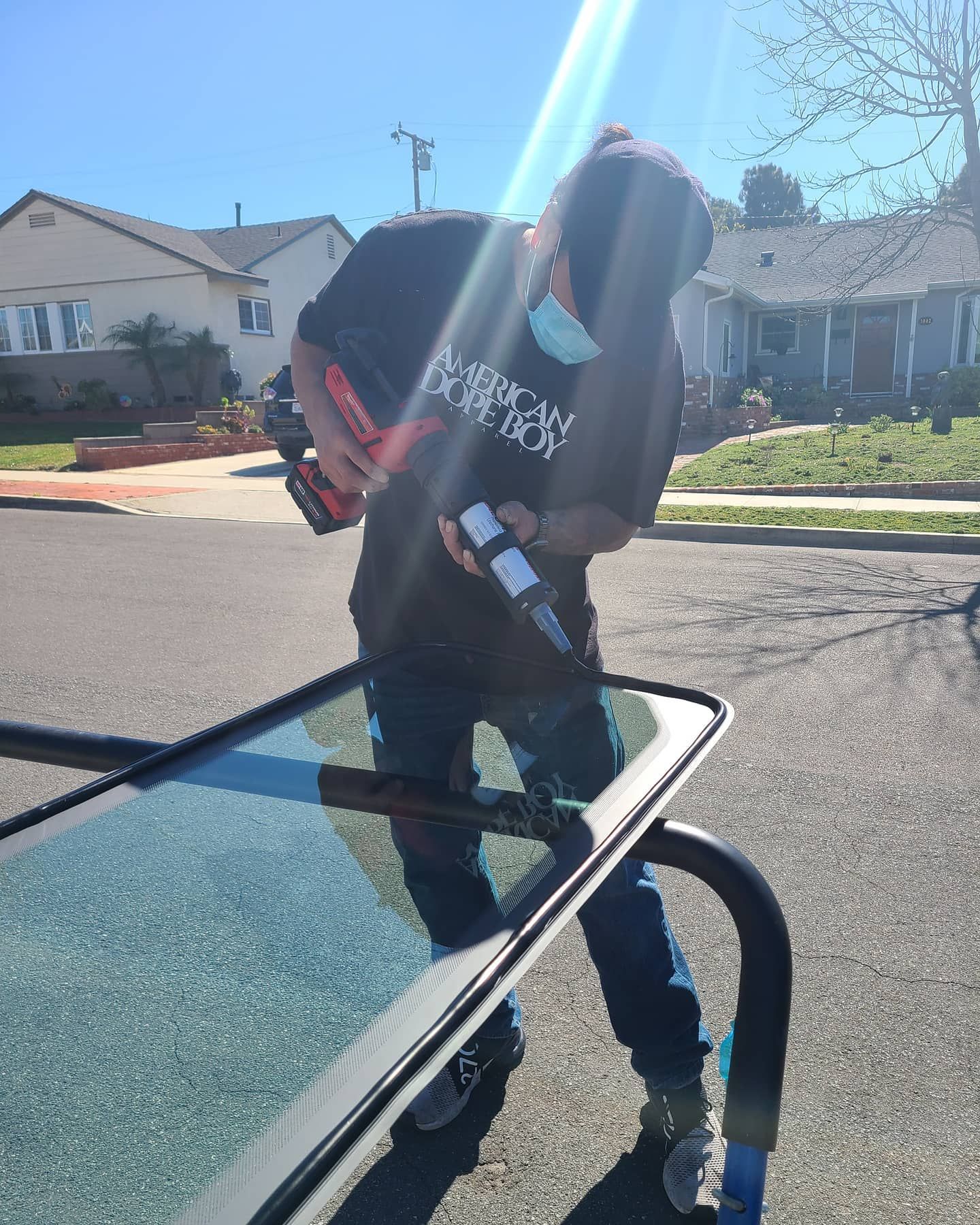 Person replacing windshield, holding tools outside, sunny day.