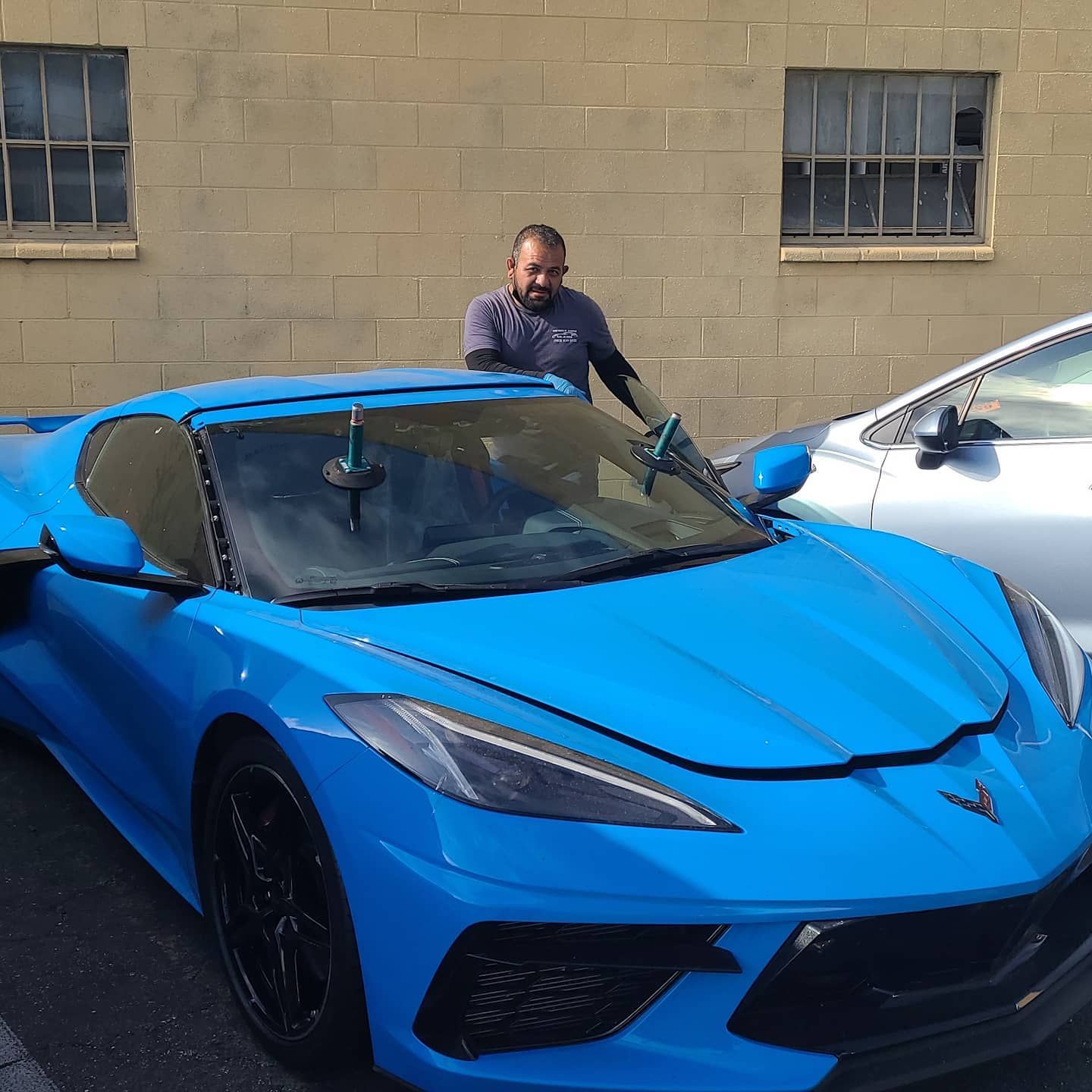 Man washing a bright blue sports car. Brick building in the background.