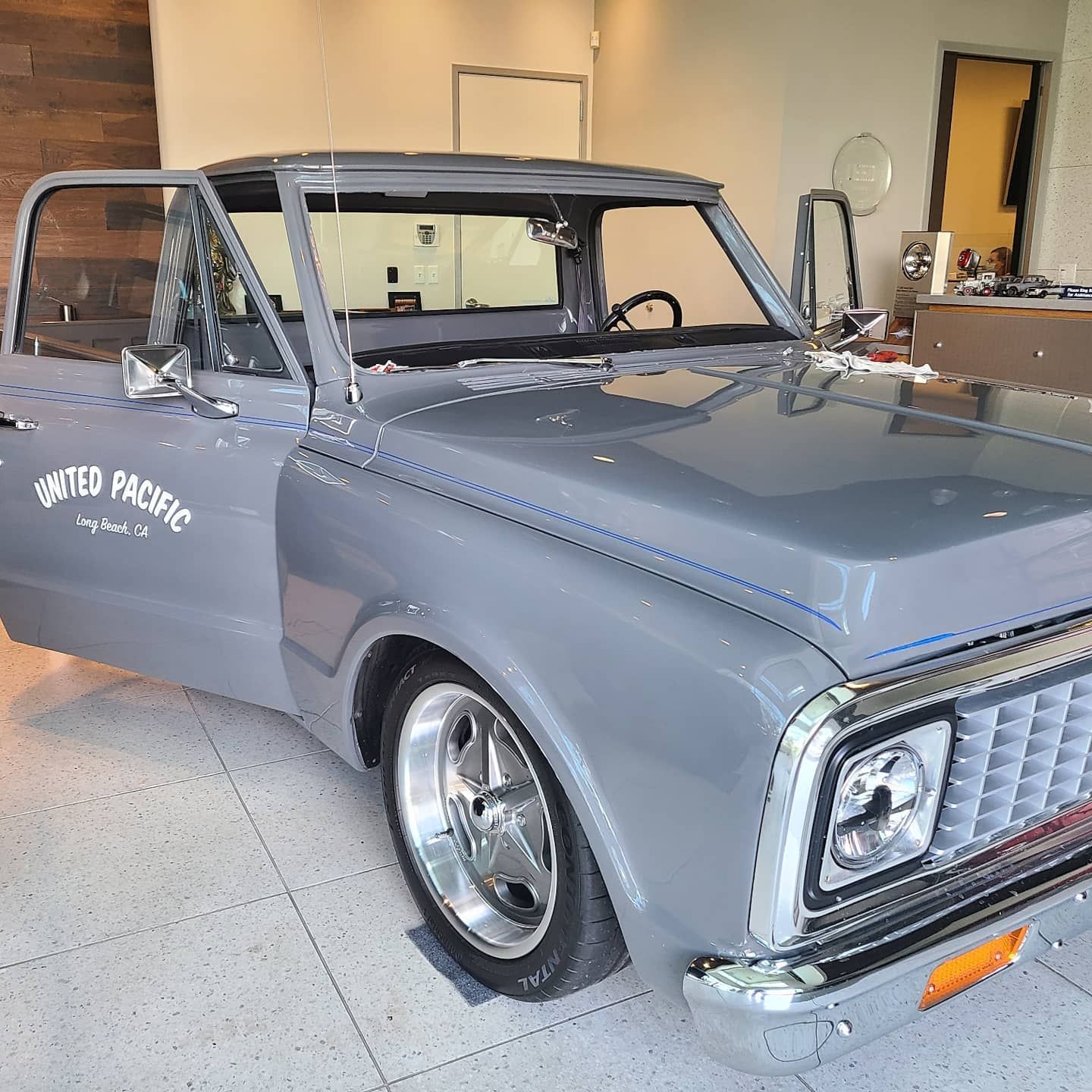 Gray classic pickup truck with chrome accents and open doors parked indoors.