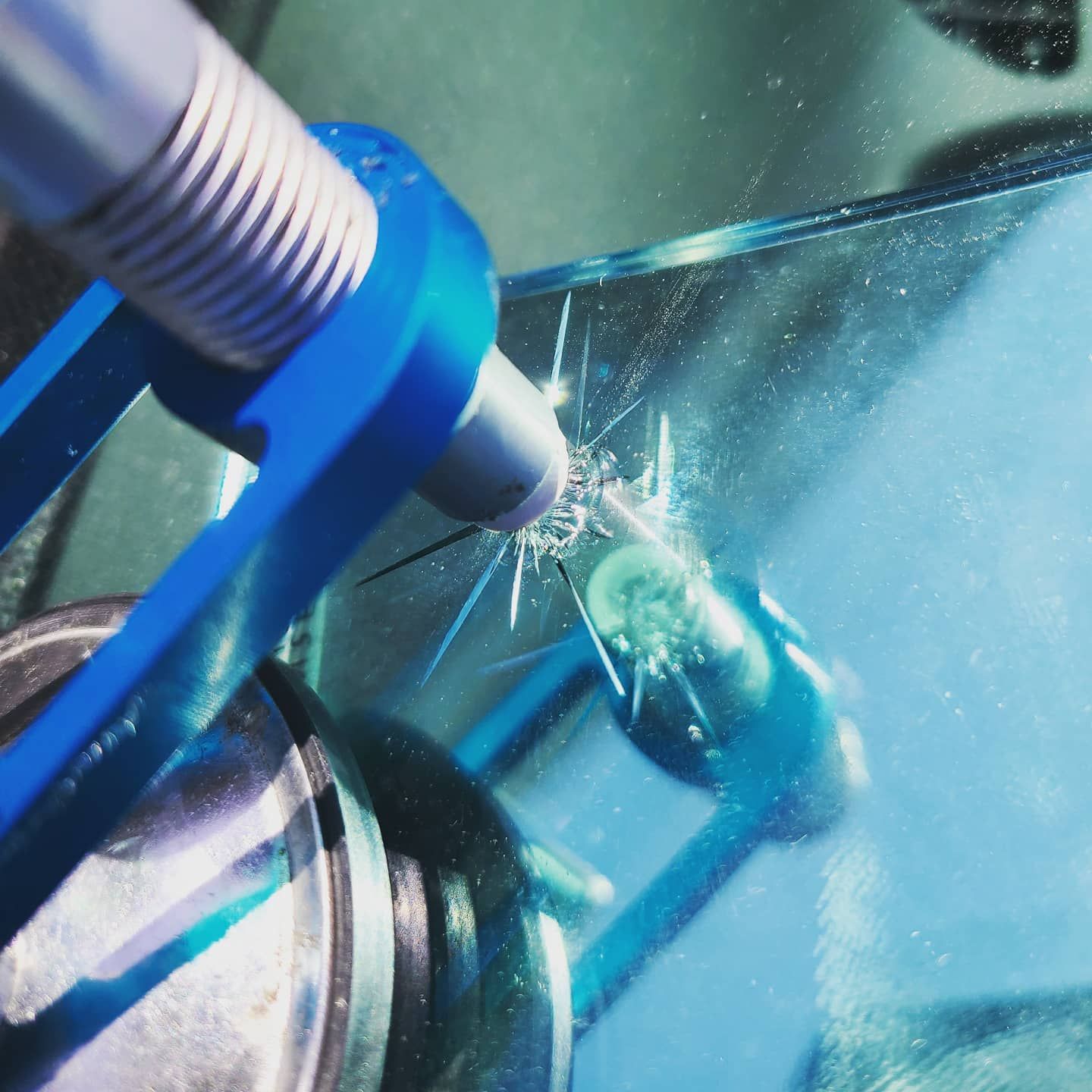 A repair tool injects resin into a damaged car windshield, filling a star-shaped crack.