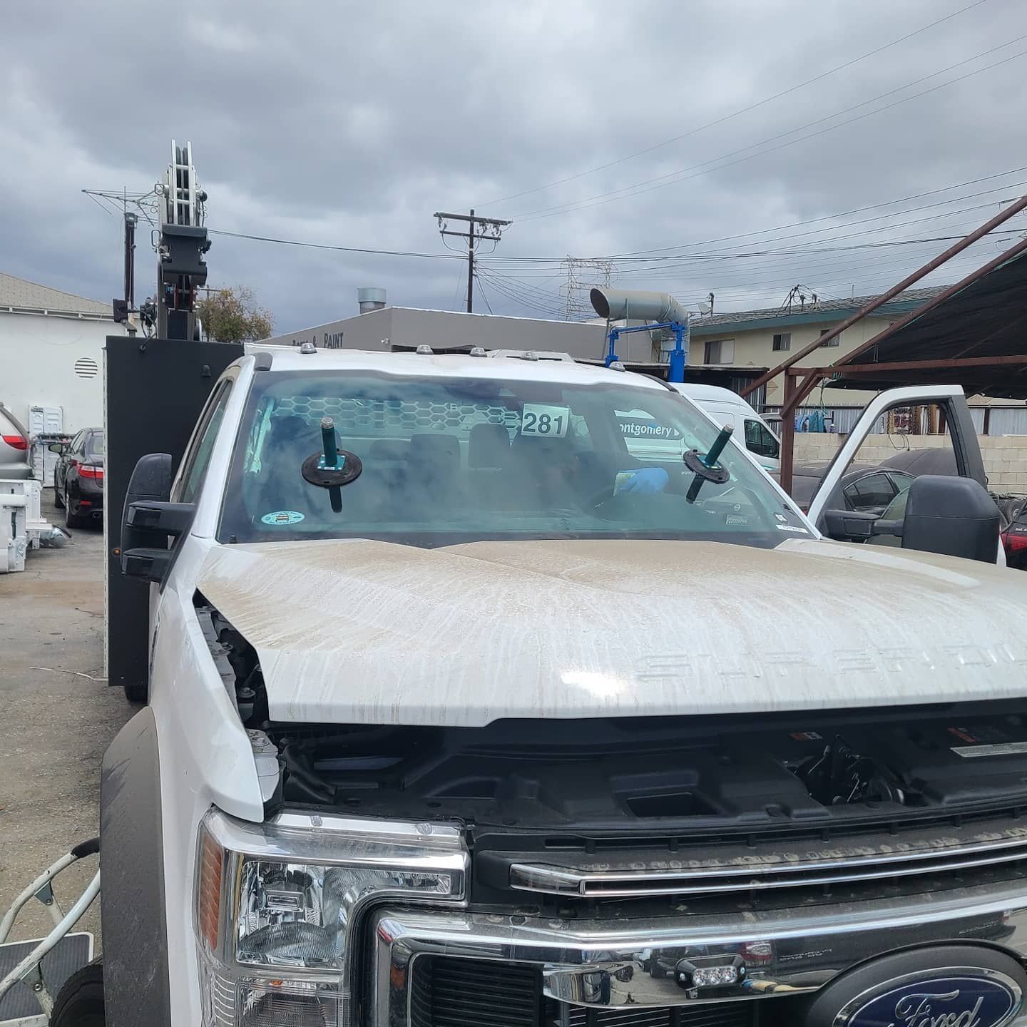 White work truck with open hood, suction cups on windshield, parked outdoors.