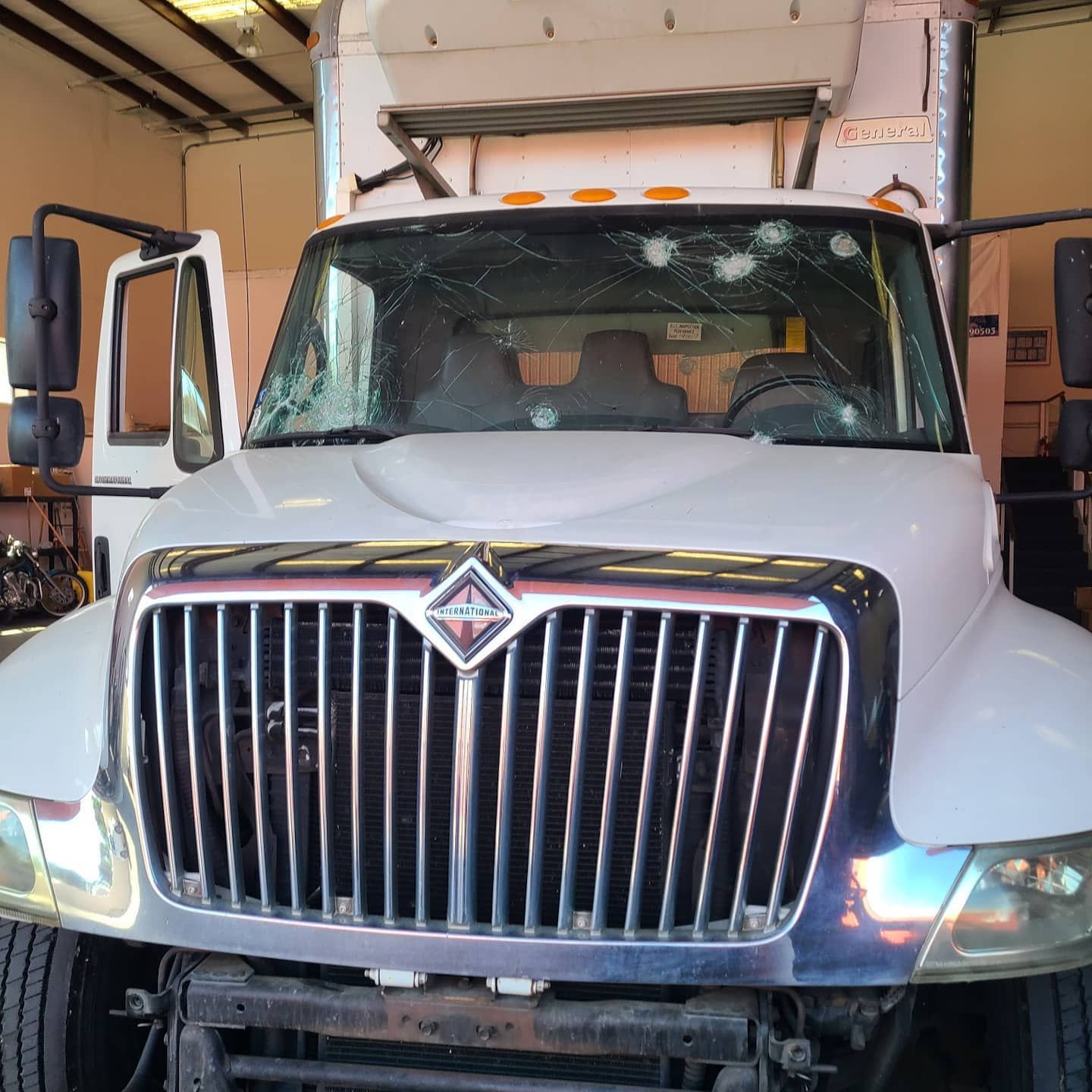 White truck with a damaged windshield and open doors. Front view, in a garage.