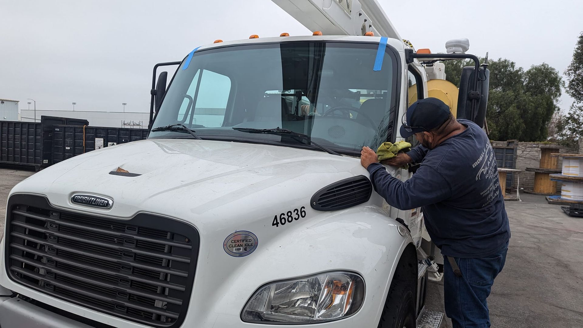 A person cleaning the windshield of a white work truck outdoors on a cloudy day.