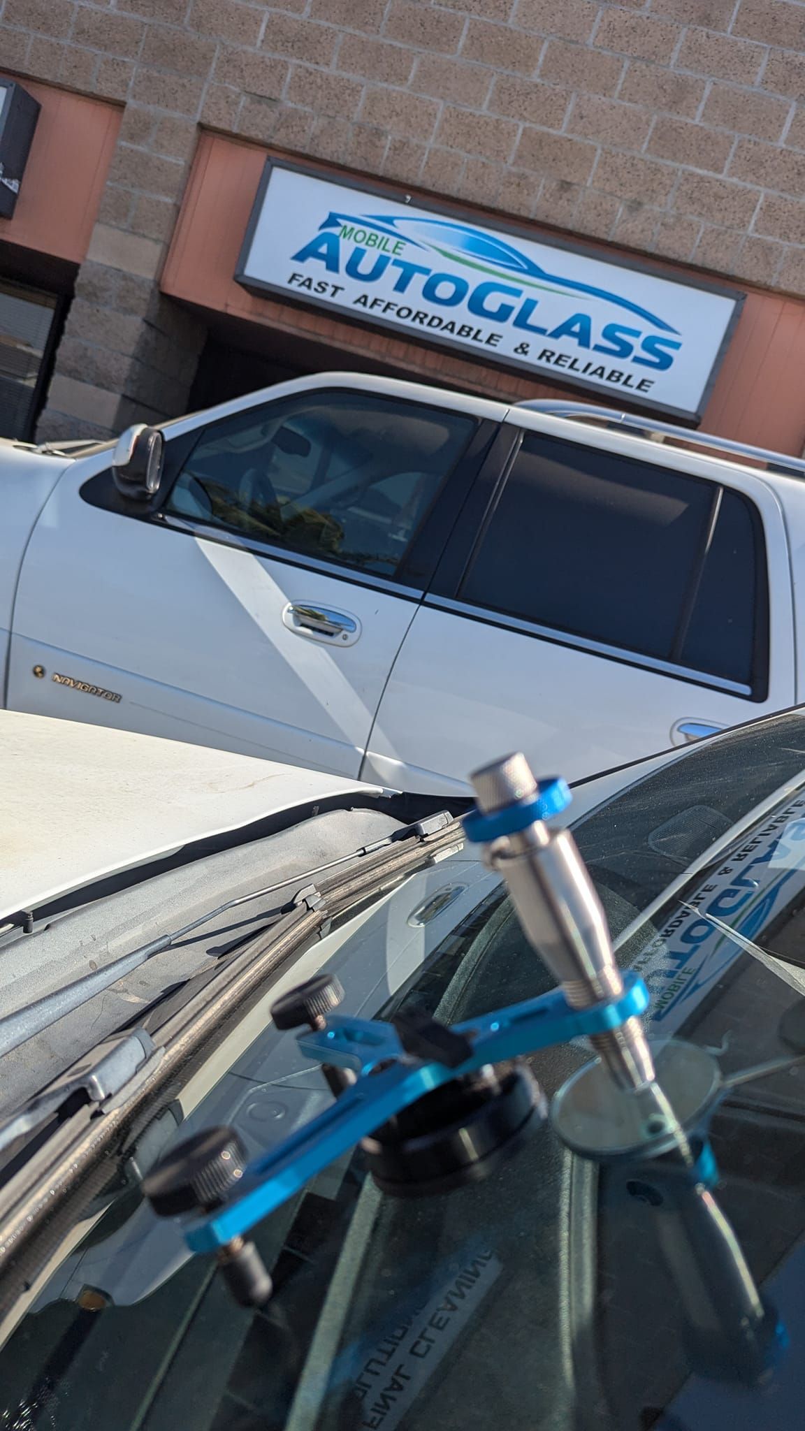 A windshield repair tool in use on a car, with an auto glass repair shop in the background.