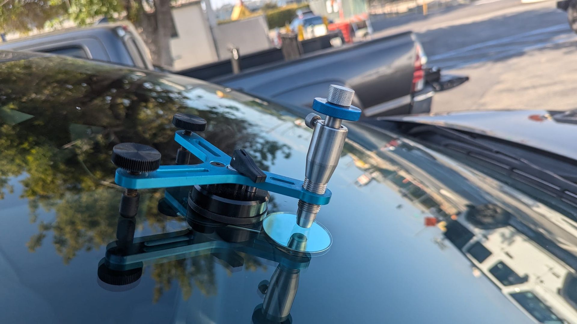 Blue windshield repair tool attached to a car's windshield. Outdoor setting, other vehicles visible.