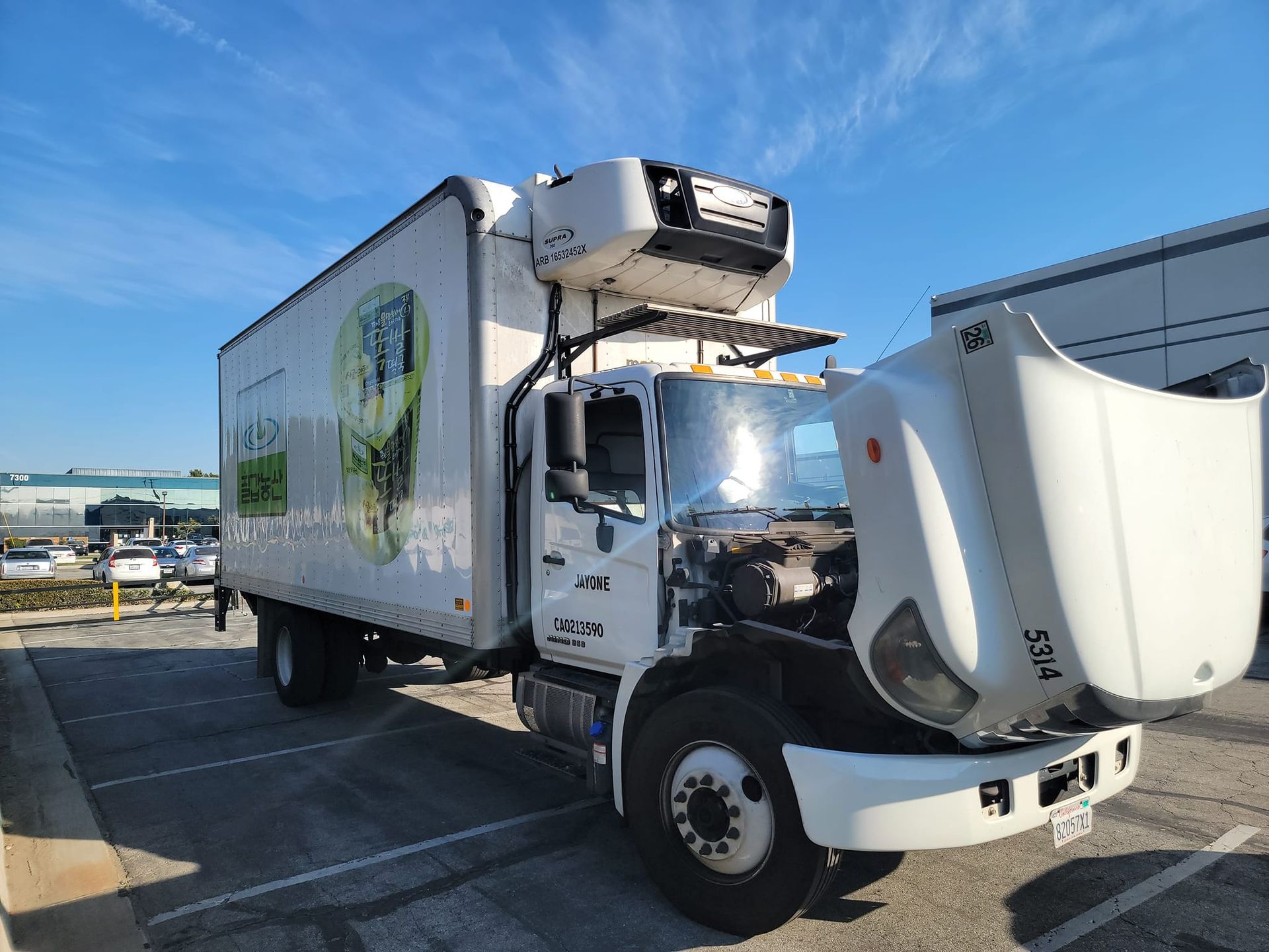 White refrigerated truck with open hood parked outside on a sunny day.