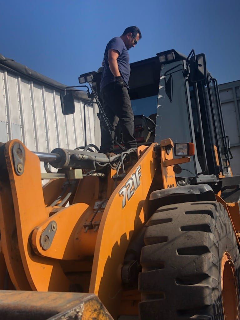 Person standing on top of an orange loader machine, blue sky background.