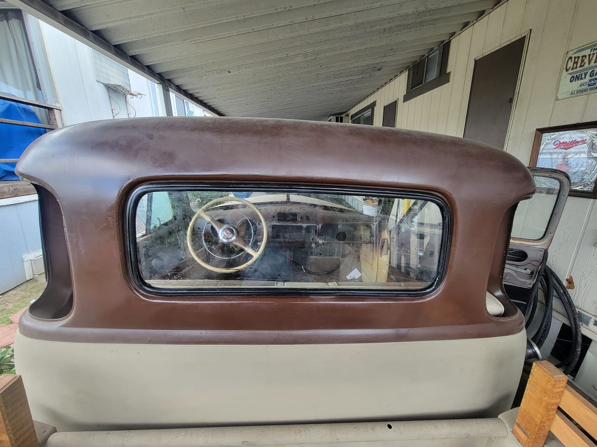 Rear section of a classic car, brown roof, tan body, visible dashboard, weathered appearance.