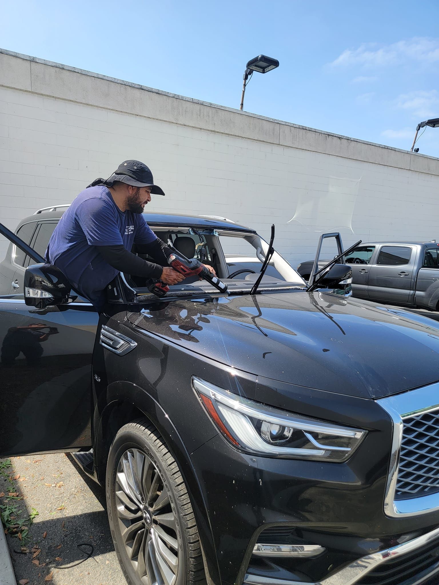 Person replacing windshield on black SUV outdoors.