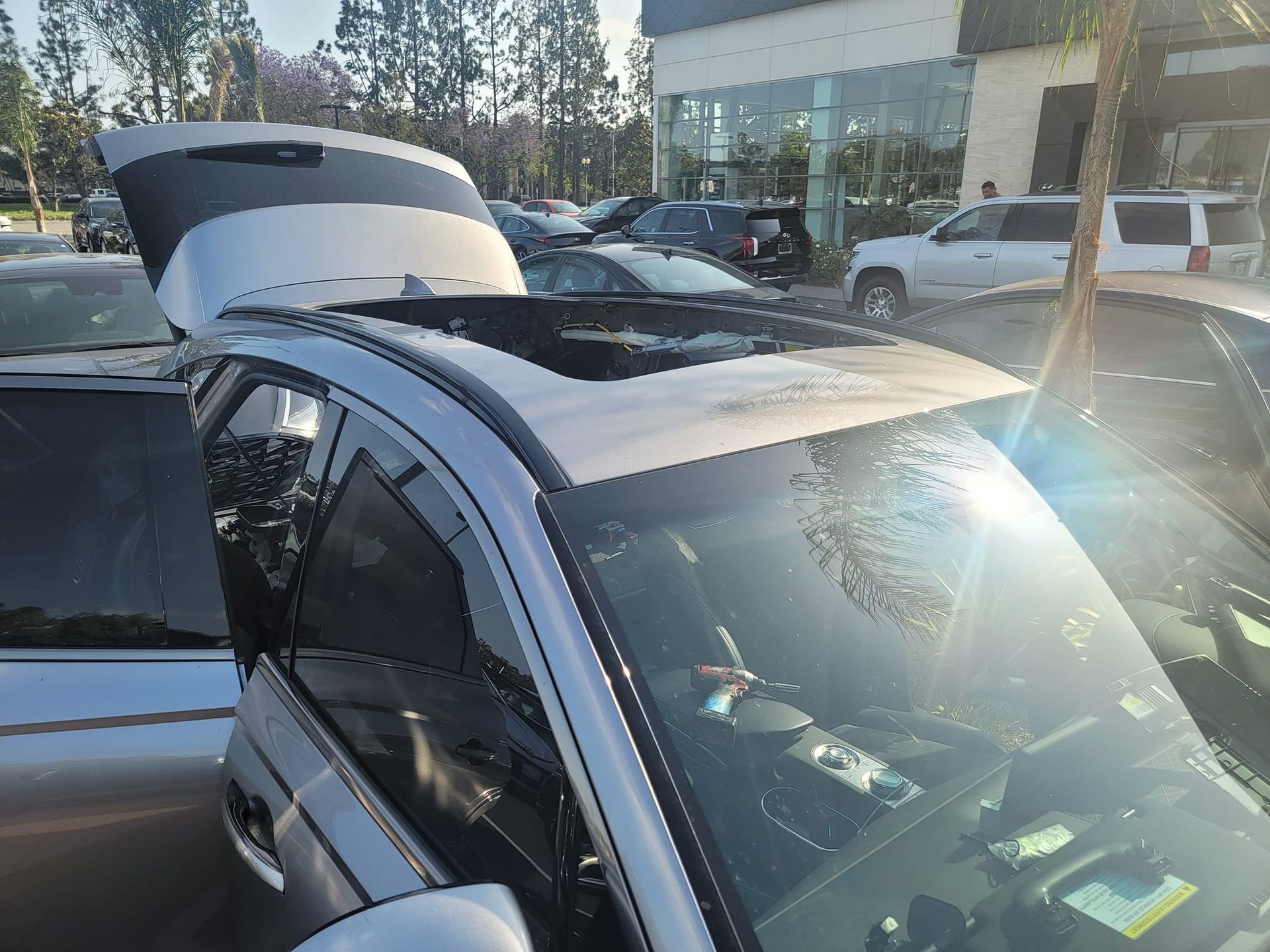 Silver SUV with open sunroof, parked in a lot, sunlight.