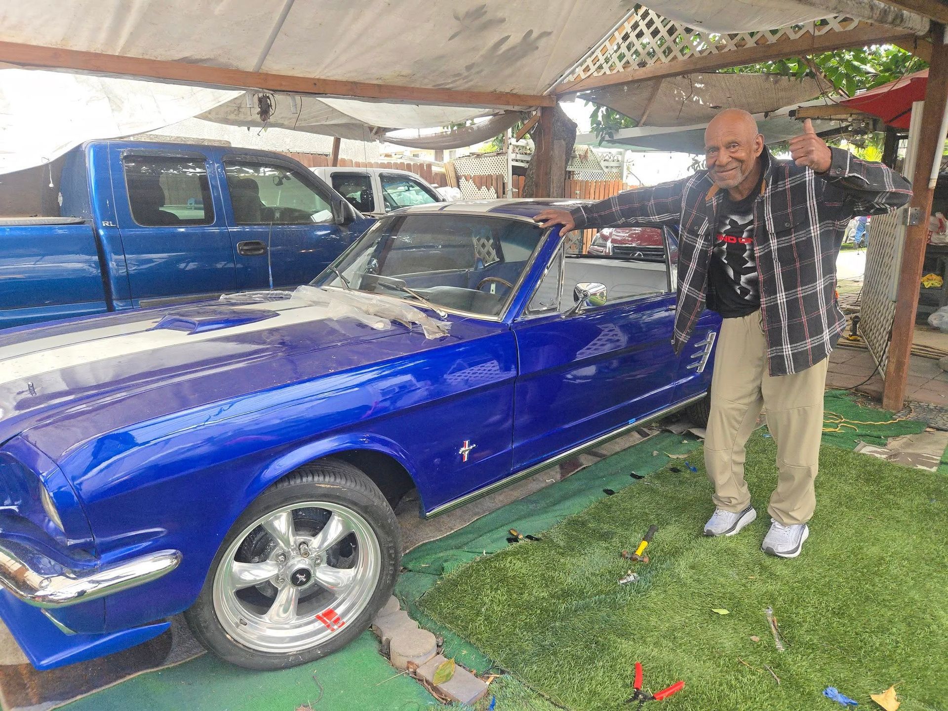 Man giving a thumbs up next to a blue classic Mustang car parked outdoors.