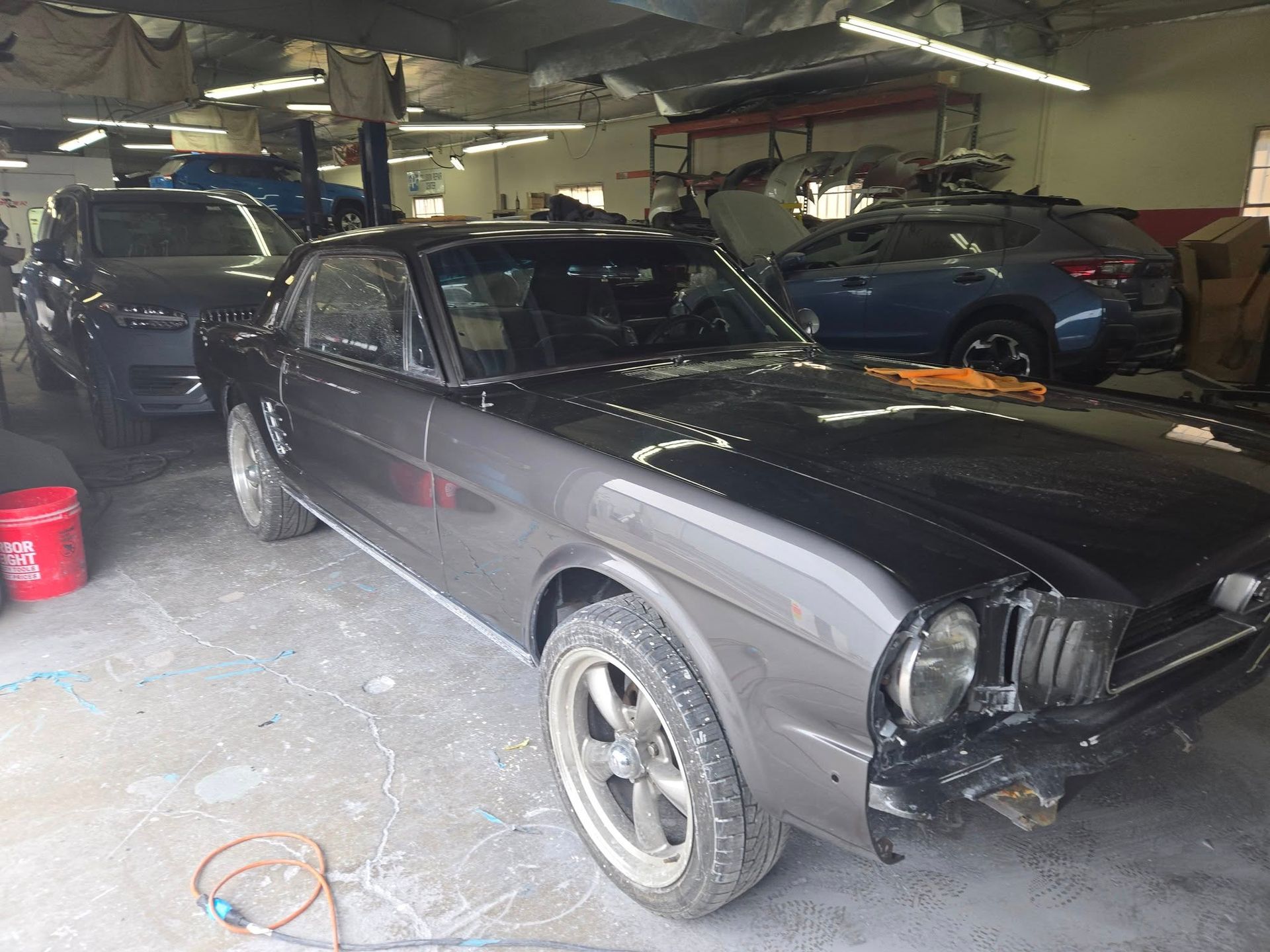 Classic gray Mustang in a garage, with other cars in the background.