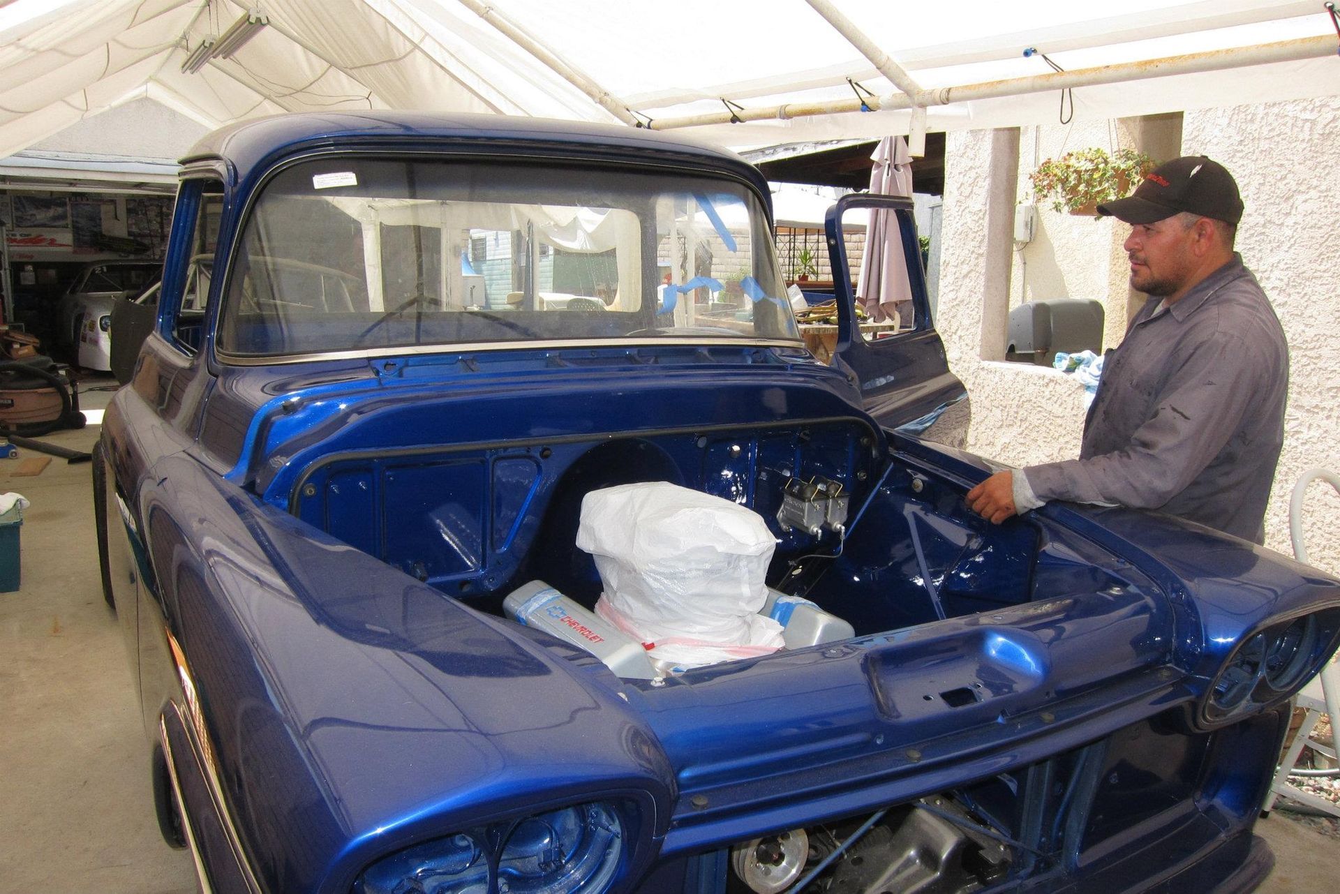 Man working on a blue classic truck in a garage; hood open, engine exposed.