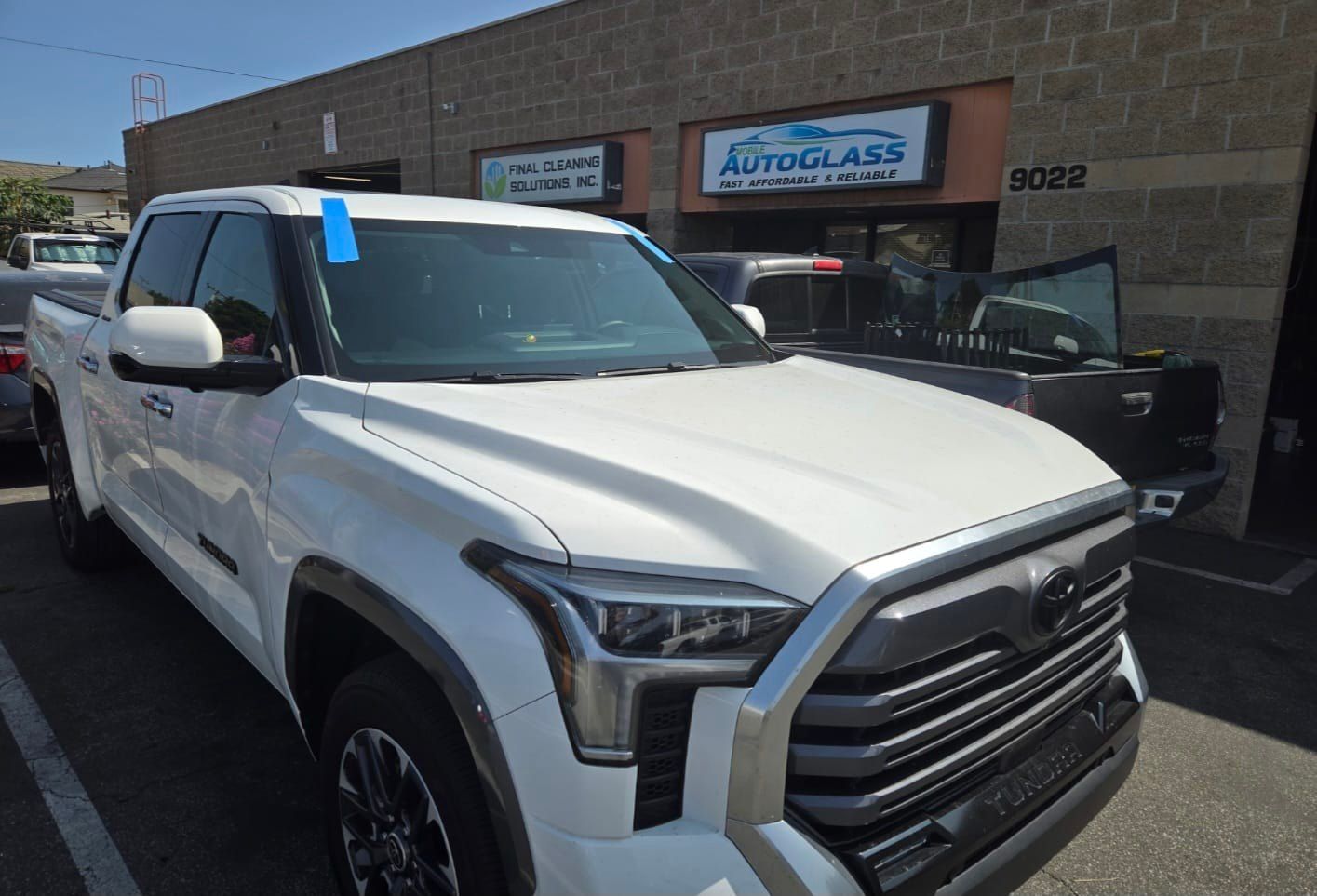 White Toyota Tundra pickup truck parked in front of an auto glass shop with a blue tape on the windshield.