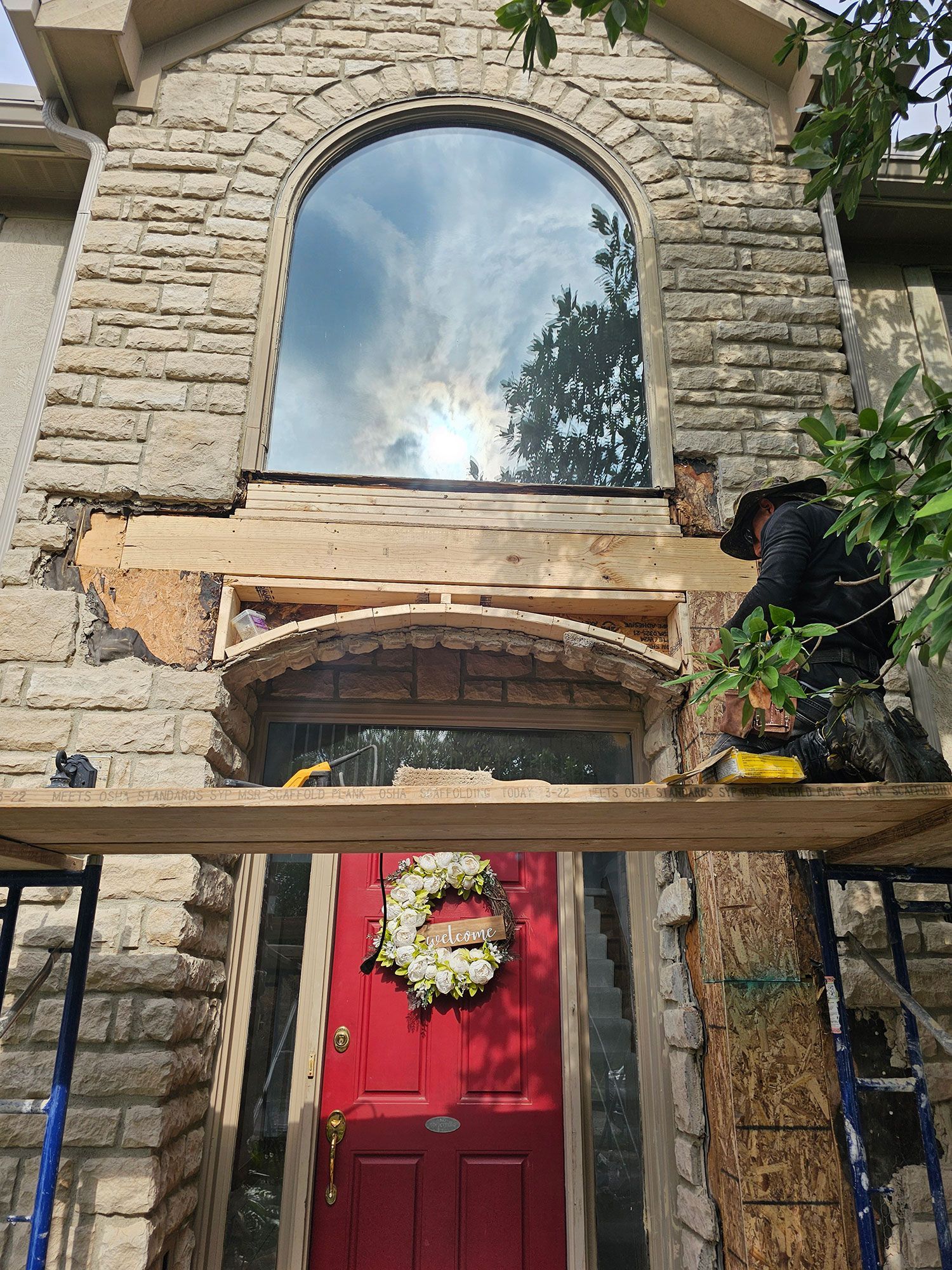 A man is working on a stone wall facade of a residential home