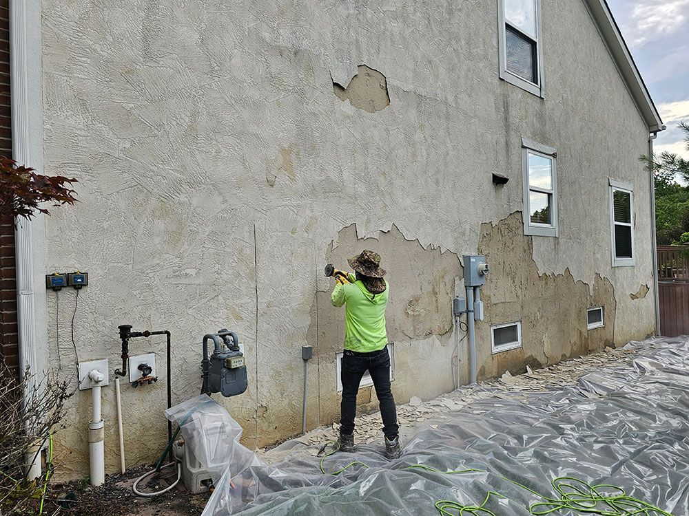 A man is stucco repairing the side of a house