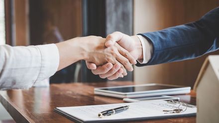 A man and a woman are shaking hands over a table.