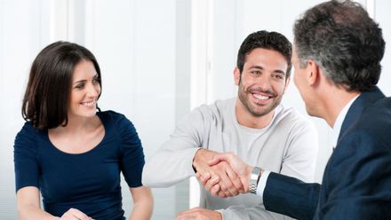 A man and a woman are shaking hands over a table.