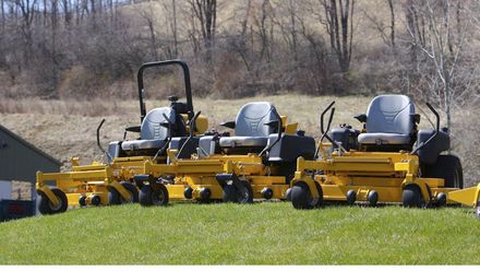 A row of yellow lawn mowers are parked in a grassy field
