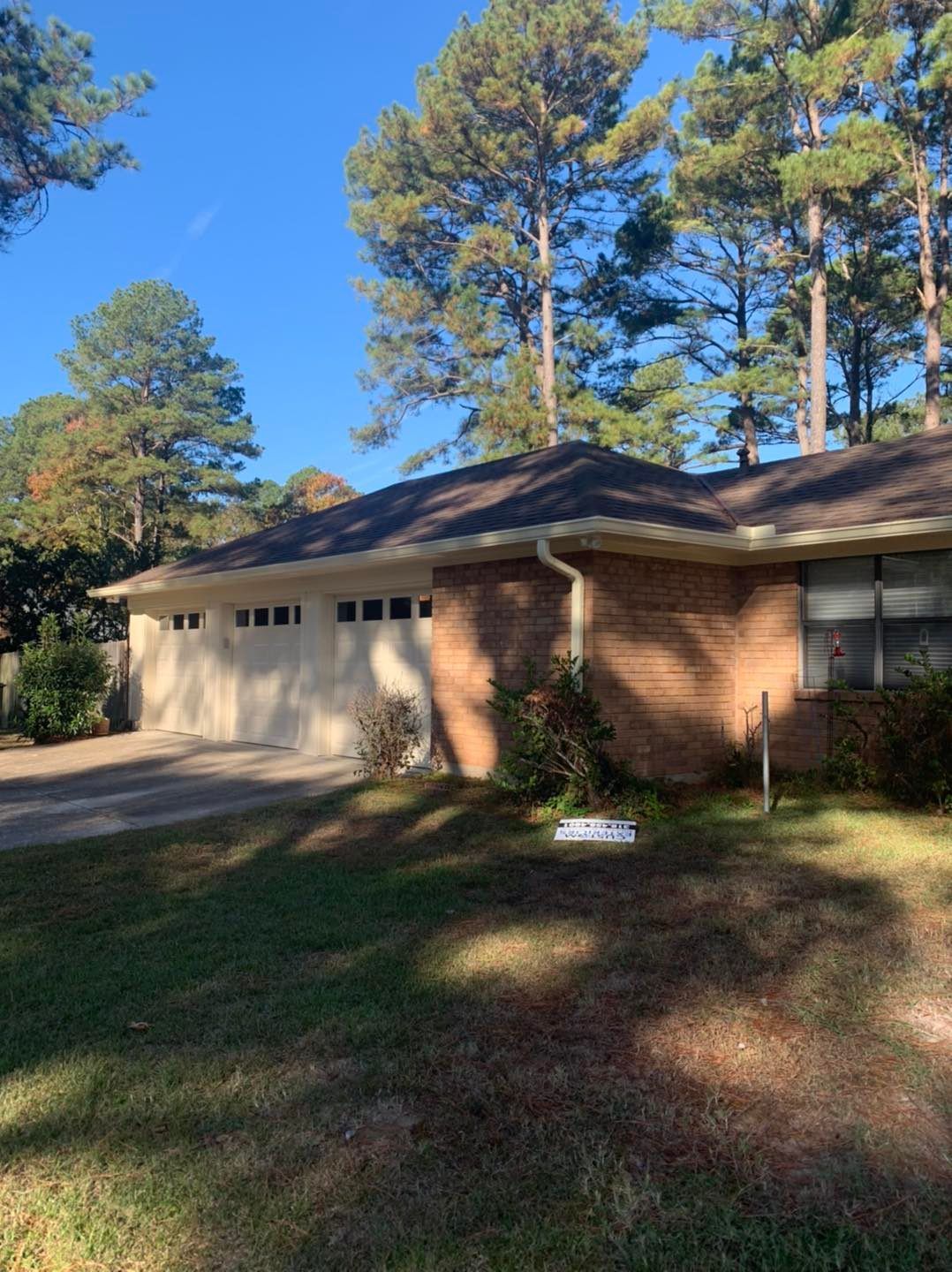 A brick house with a multi-car garage, surrounded by tall pine trees under a clear blue sky.