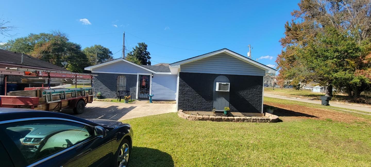 A single-story house with black brick siding and white trim under a clear blue sky, seen from a grassy yard.