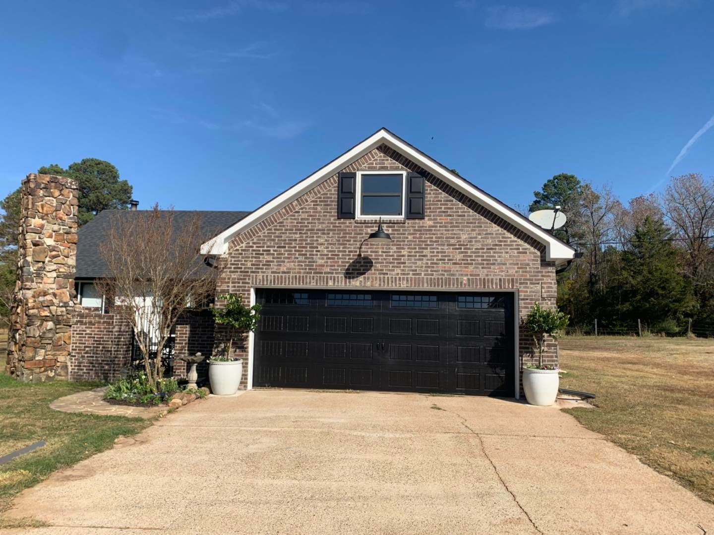 A brown brick house with a dark garage door, a stone chimney, and a small attic window under a clear blue sky.